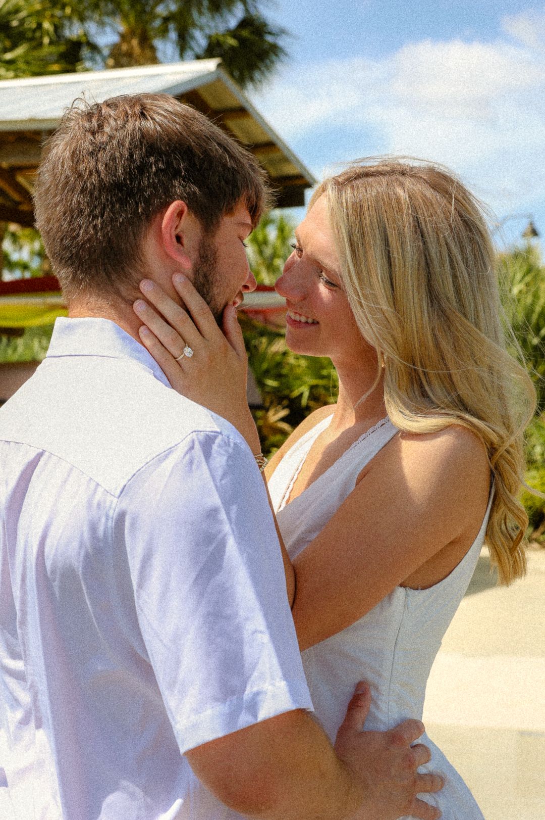 A joyful couple nearly kissing outdoors, woman displaying an engagement ring on her hand.