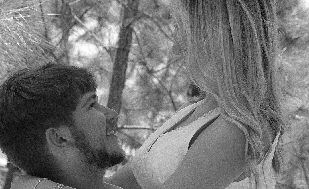 Black and white photo of a couple sharing a romantic moment among trees.