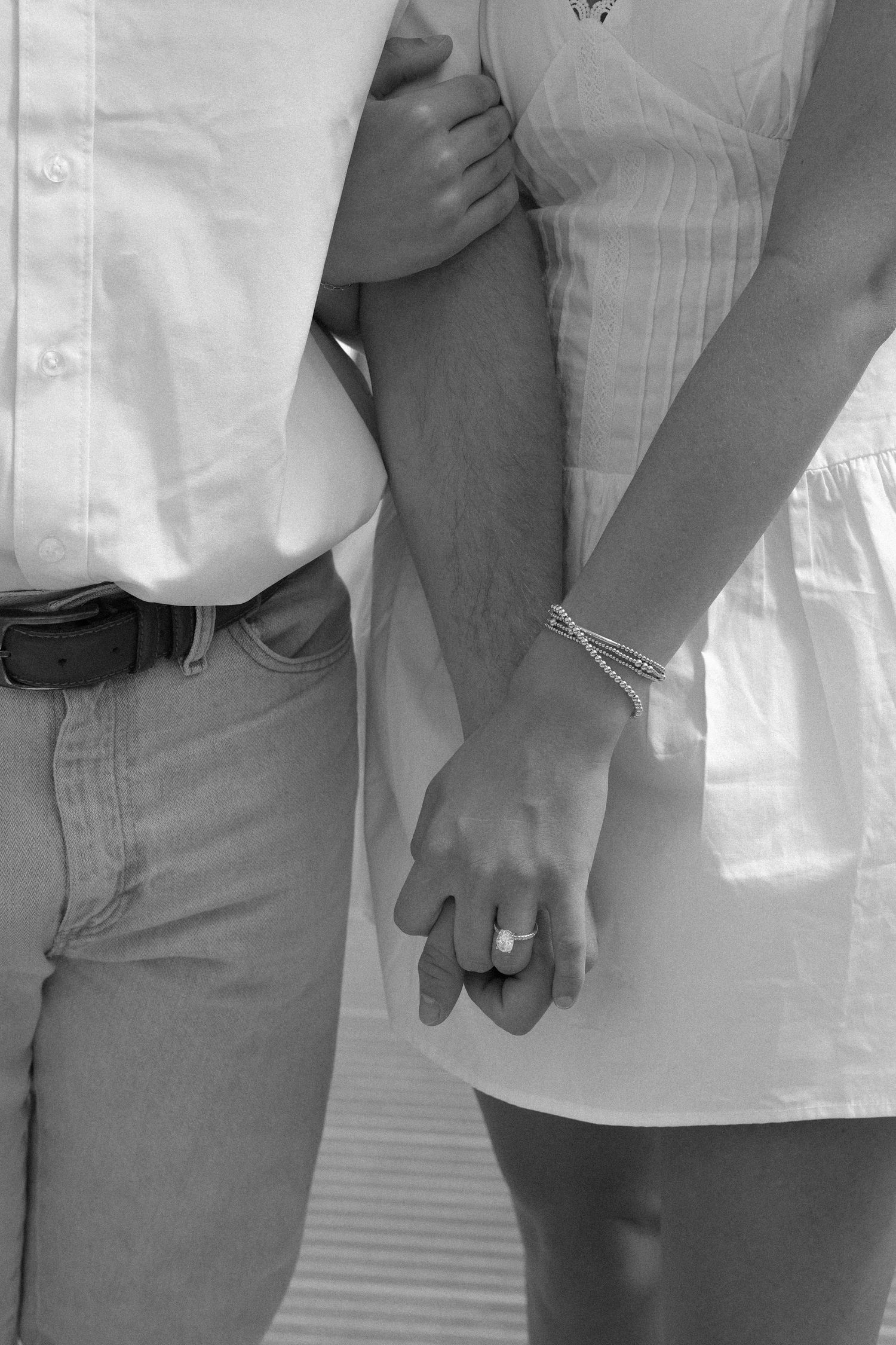 Black and white photo of a couple holding hands, woman wearing an engagement ring and bracelets.