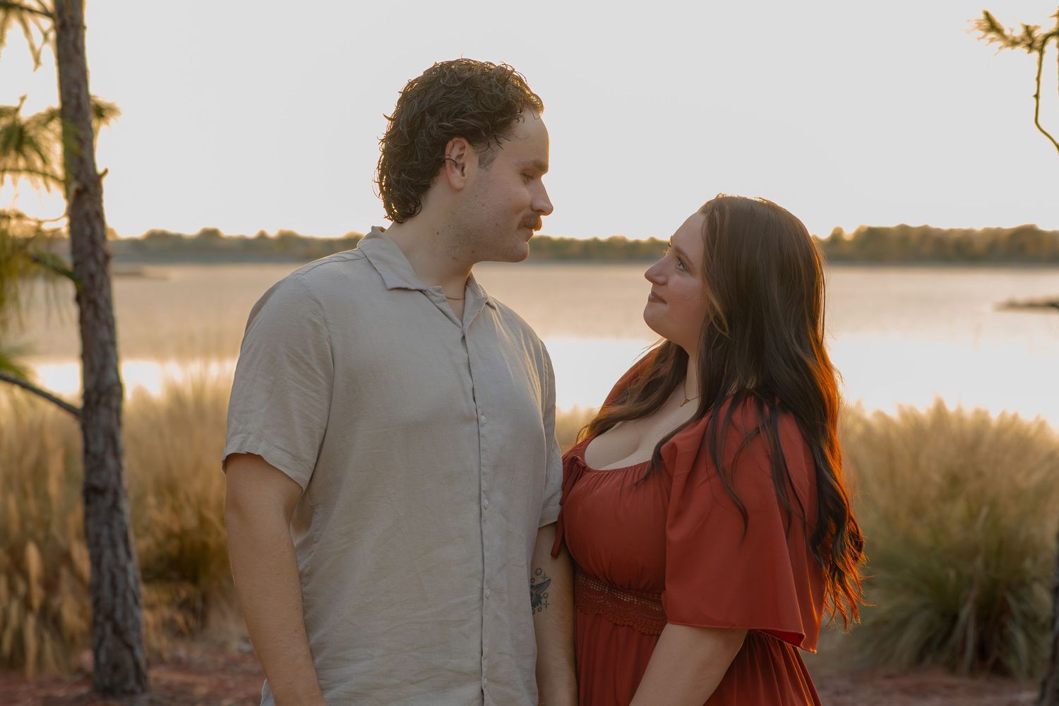 Smiling couple shares a tender moment outdoors near a lake at golden hour.