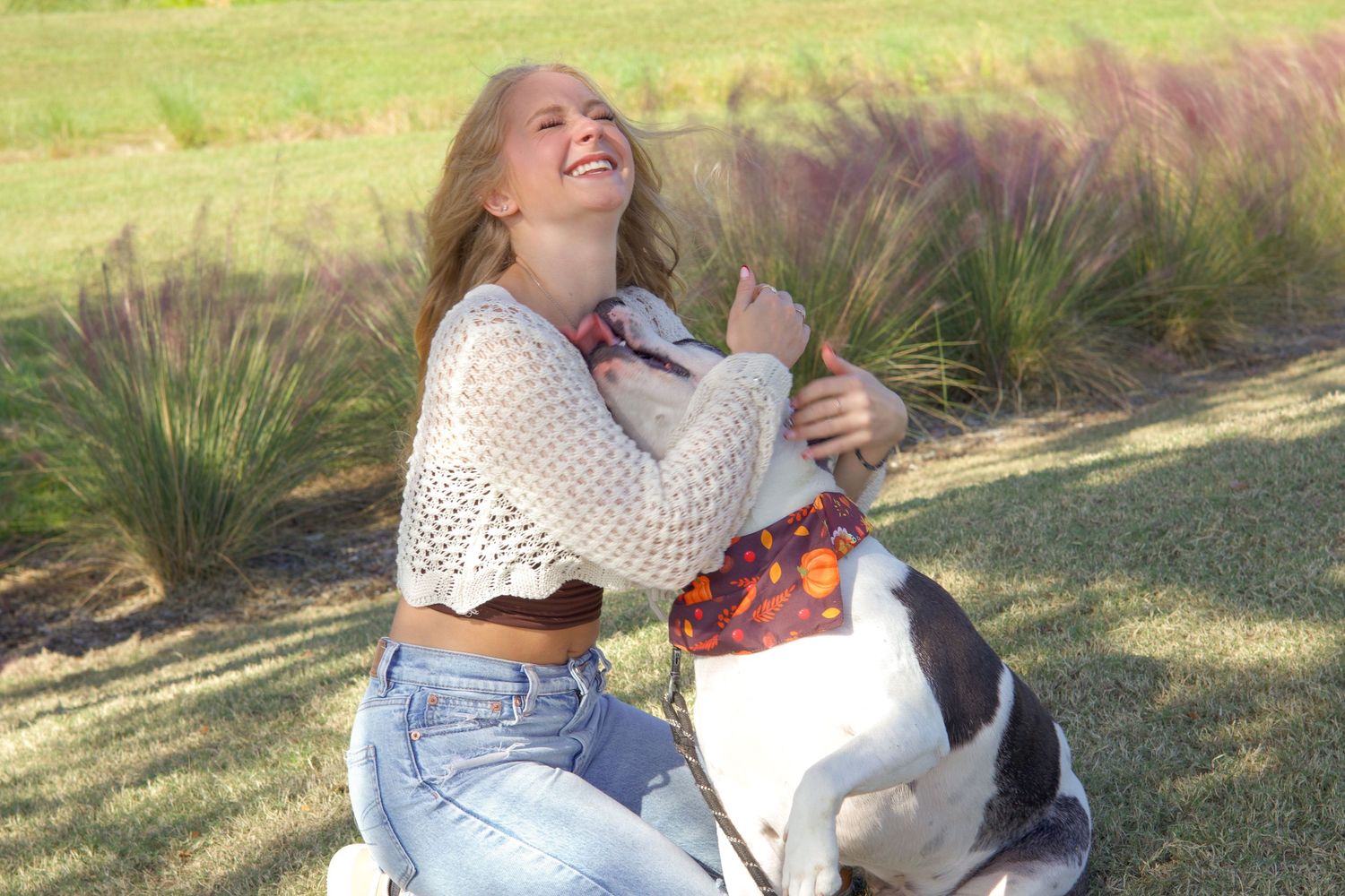 Laughing blonde woman in crochet top hugging white and black dog in park.