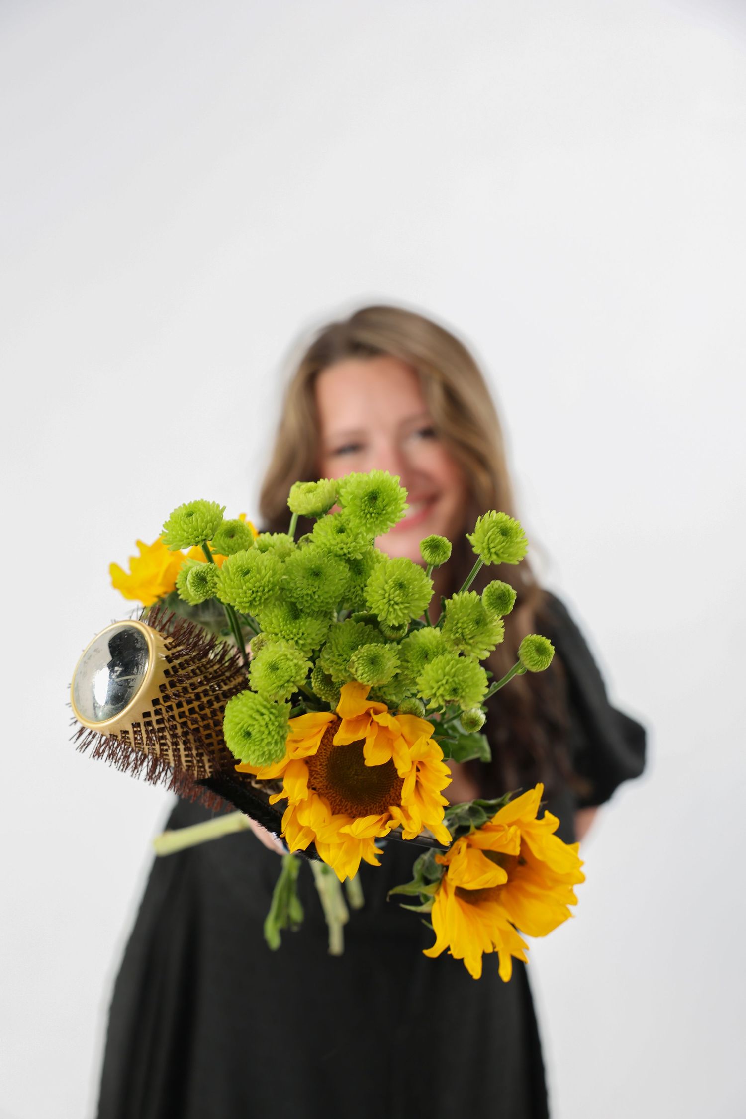 Woman in black dress extending a bouquet of sunflowers and green flowers toward the camera.