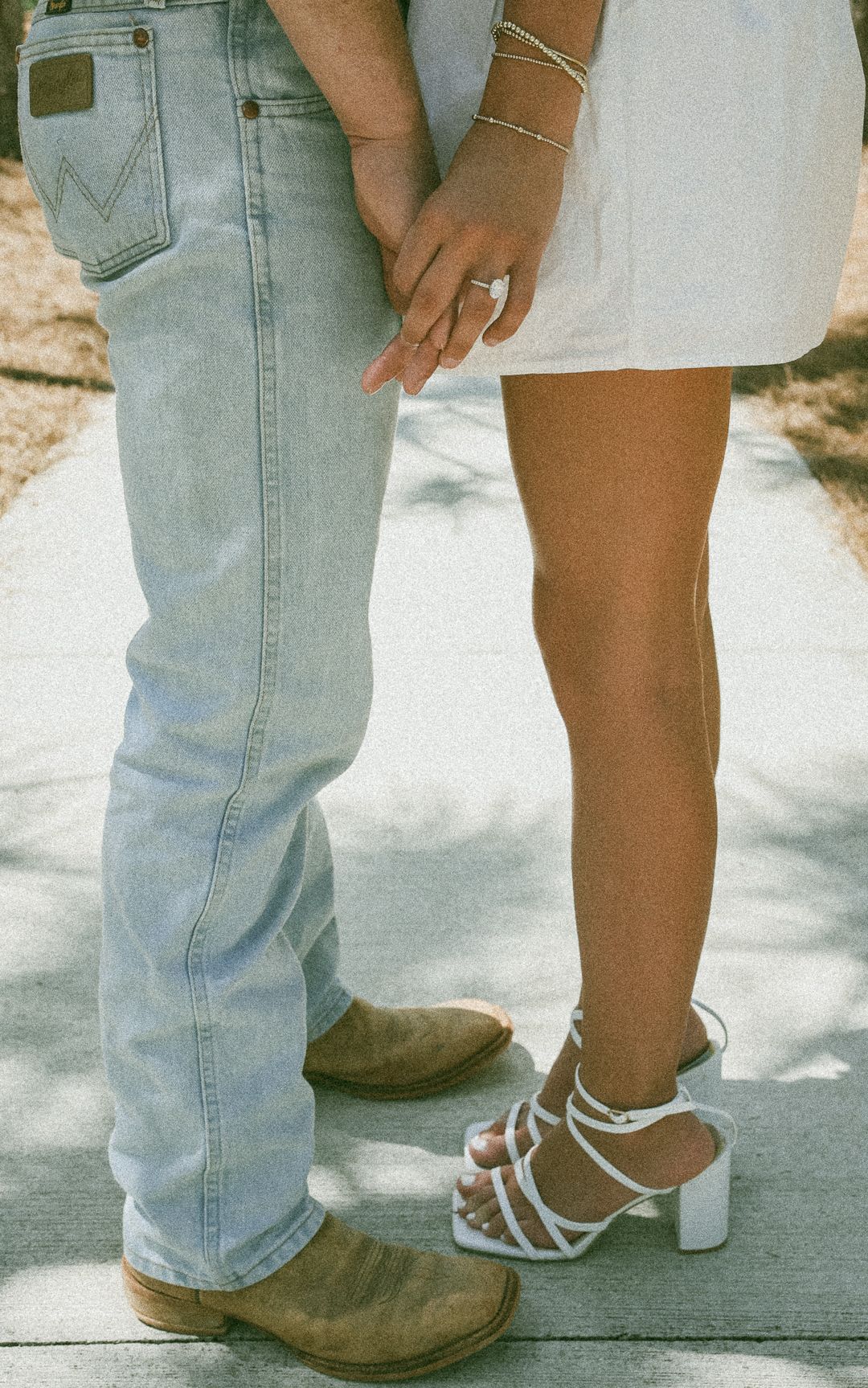 Couple holding hands, man in Wrangler jeans and cowboy boots, woman in white dress and strappy heels.