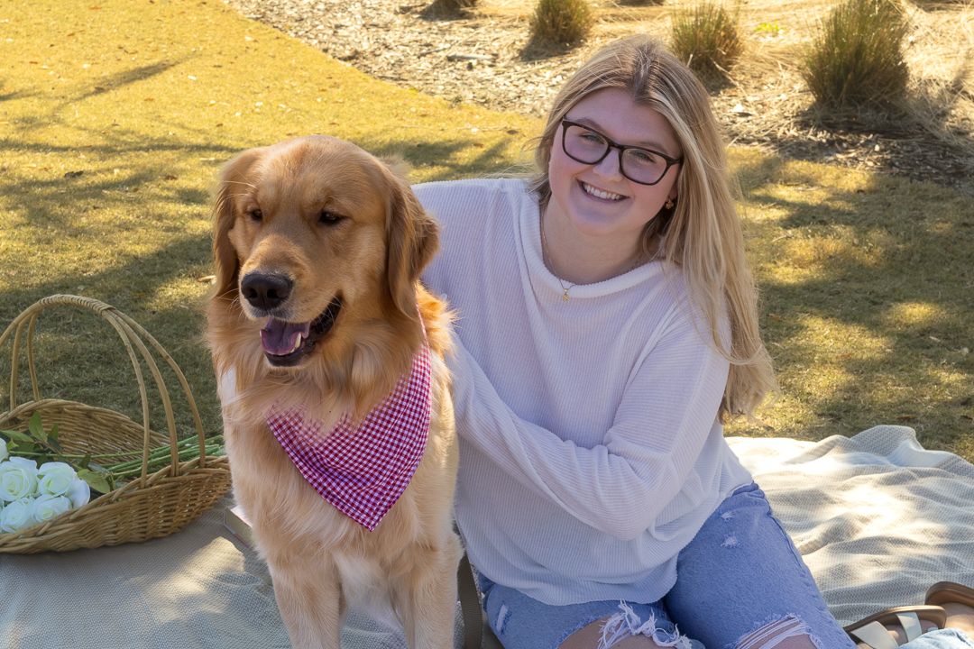 Smiling girl sitting on a picnic blanket with her Golden Retriever dog in a sunny park.