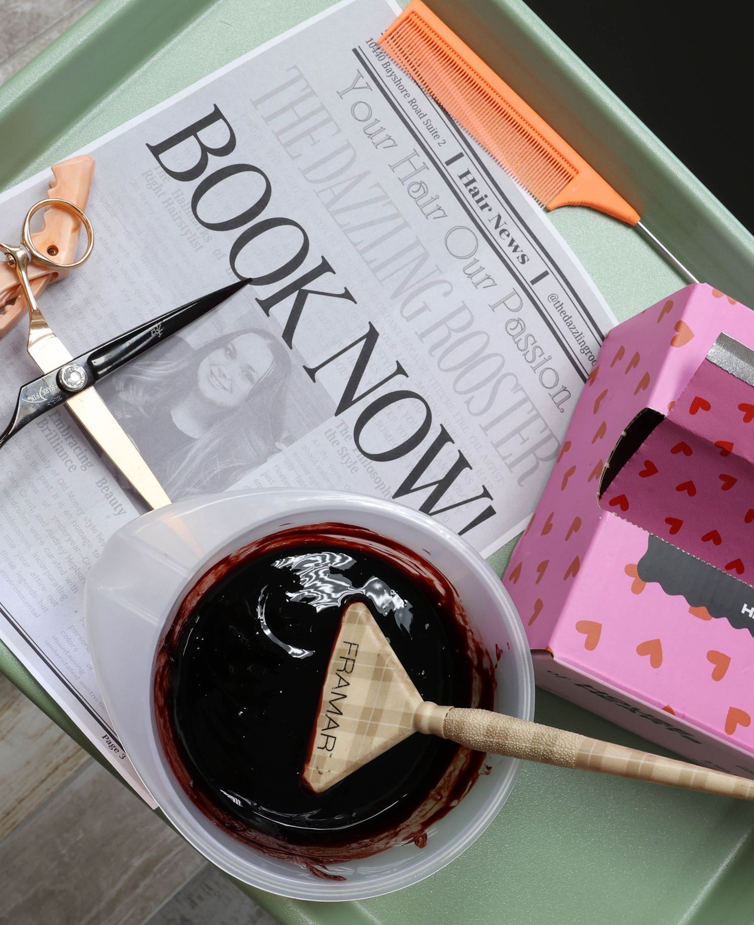 Flat lay of hair salon booking flyer, scissors, hair dye bowl, comb, and pink gift box.