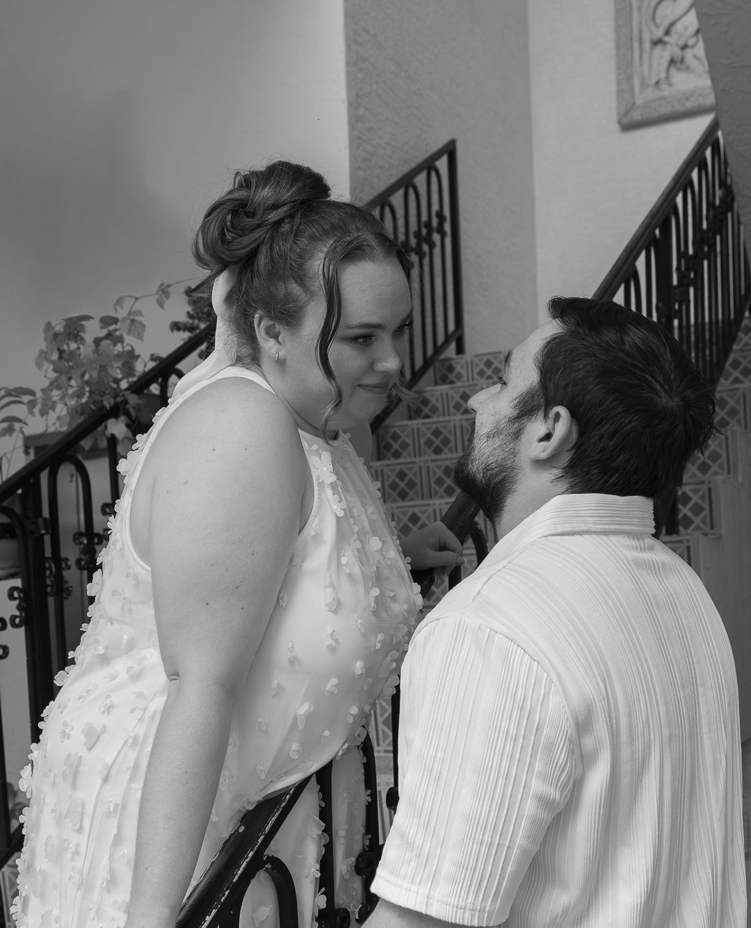 A couple shares a romantic moment on a staircase, the woman in a white dress smiling at her partner.