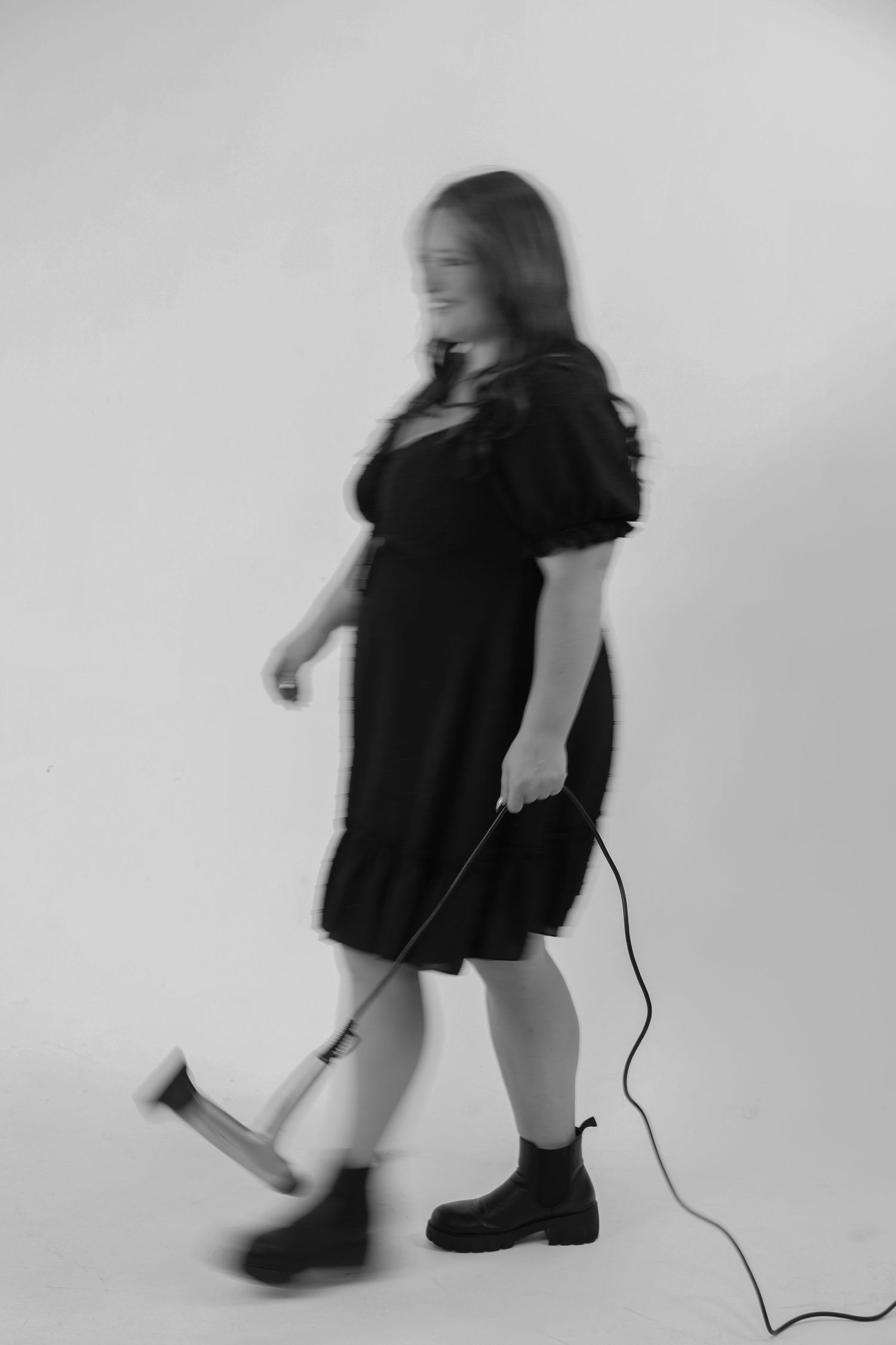 Woman in black dress walking with a hammer and cord in a blurred motion black and white photo.