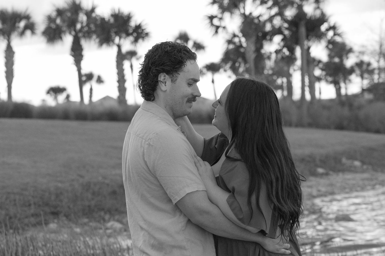 Black and white photo of couple holding each other with palm trees behind them.