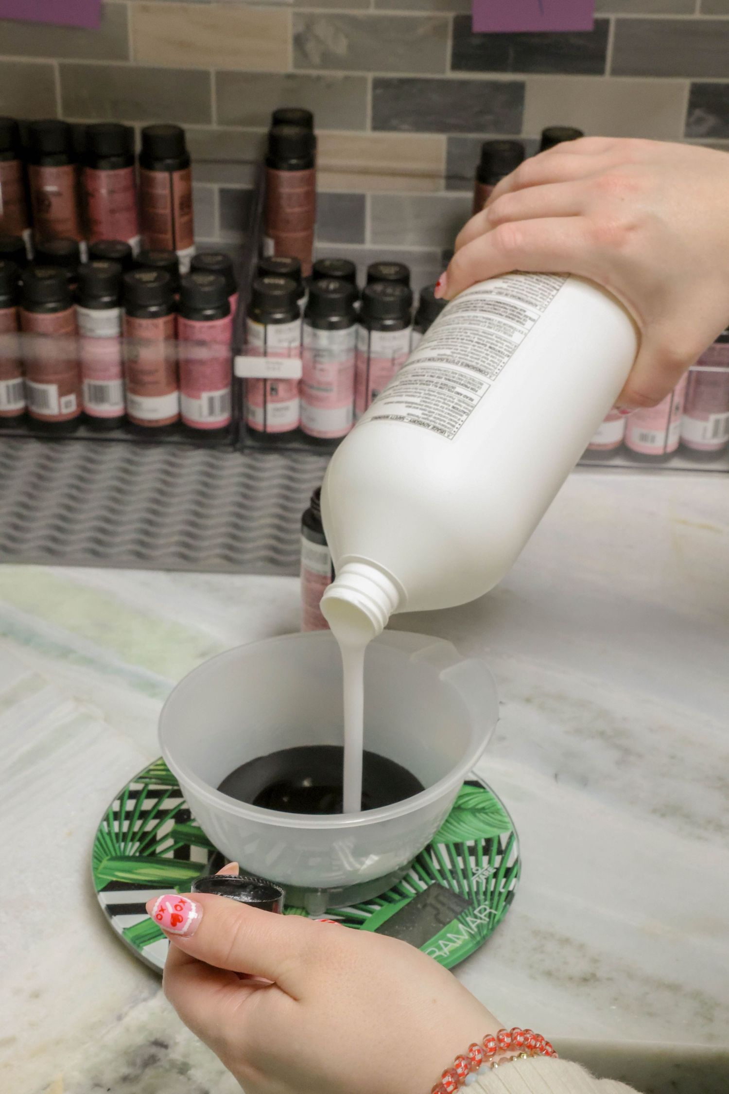 Hands pouring white hair color developer into a mixing bowl at a salon color bar.