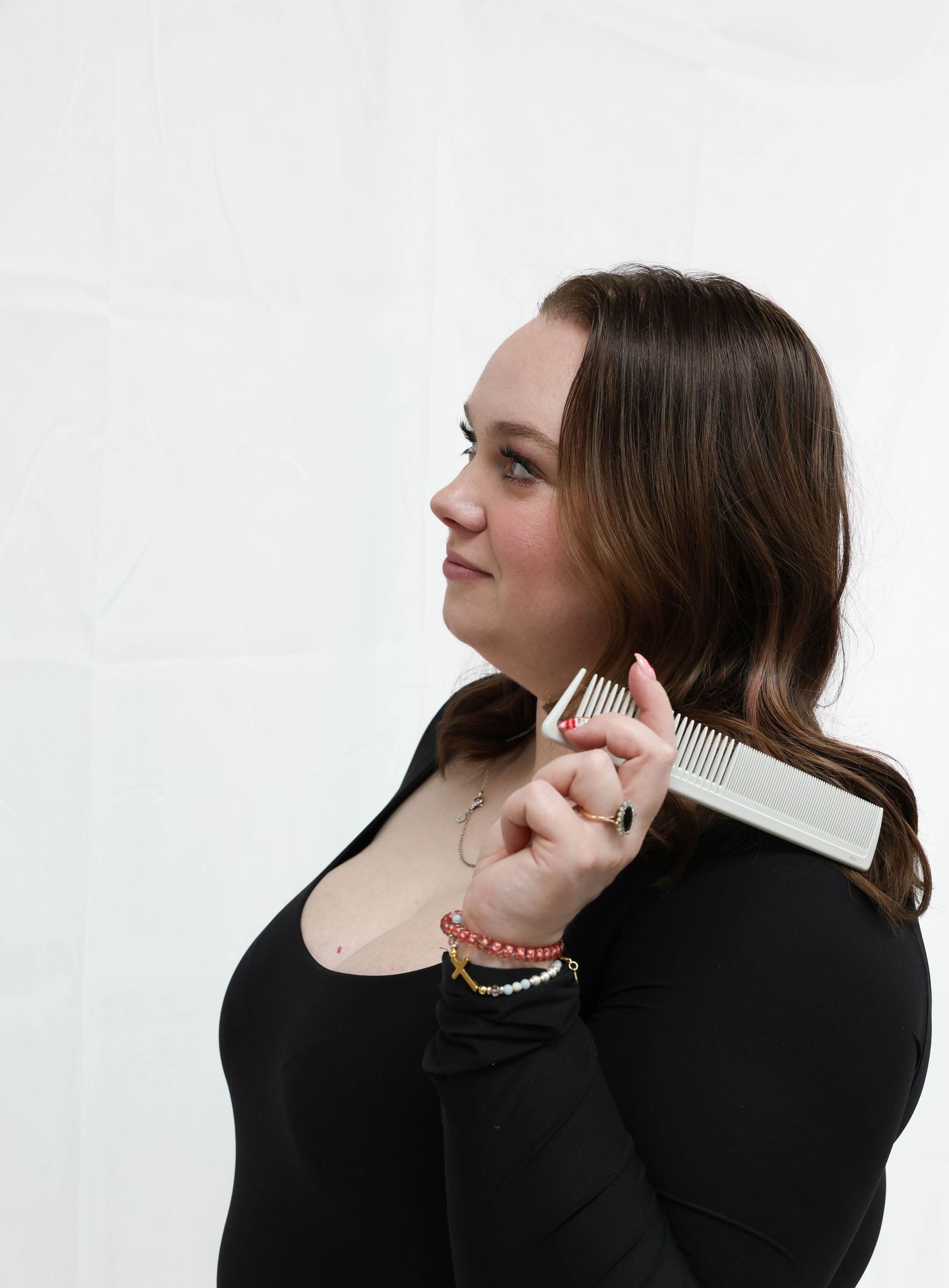 Young woman in black top combing her long brown hair against a white background.