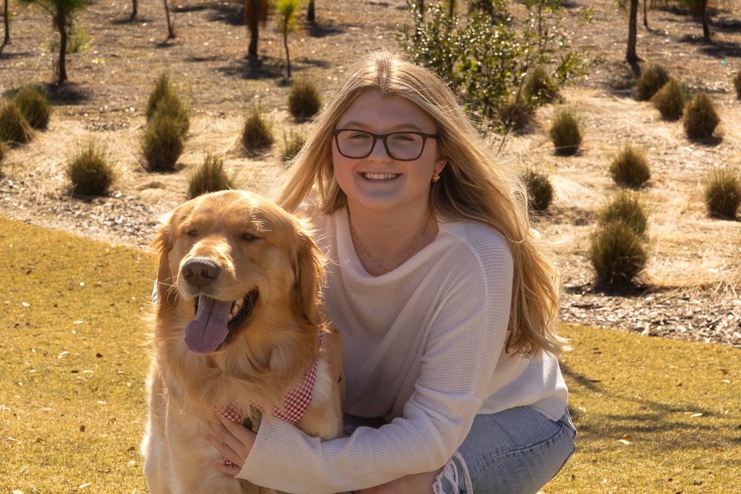 Happy blonde girl hugging her Golden Retriever dog while kneeling in a sunny park.