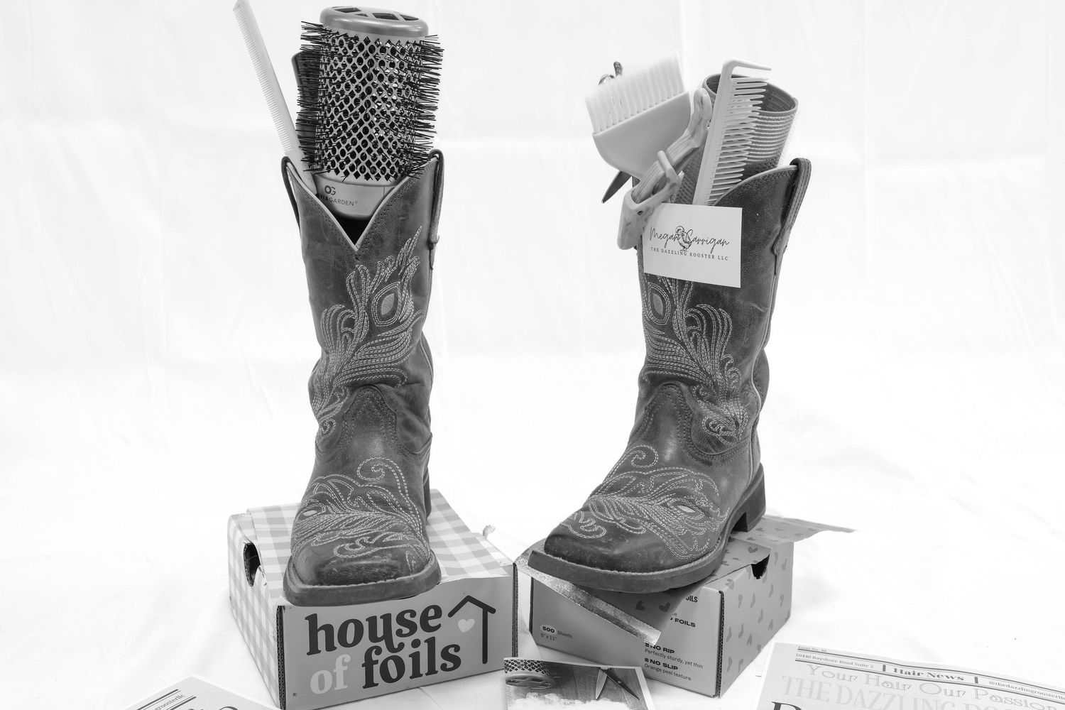 Black and white photo of cowboy boots filled with hair styling tools on House of Foils boxes.