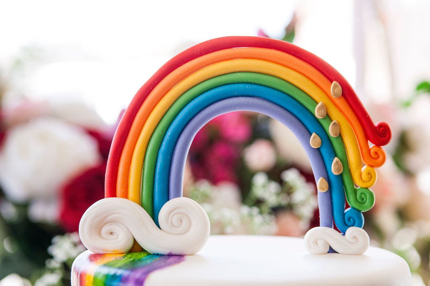 Colorful rainbow cake topper made of fondant with white clouds on a white cake.