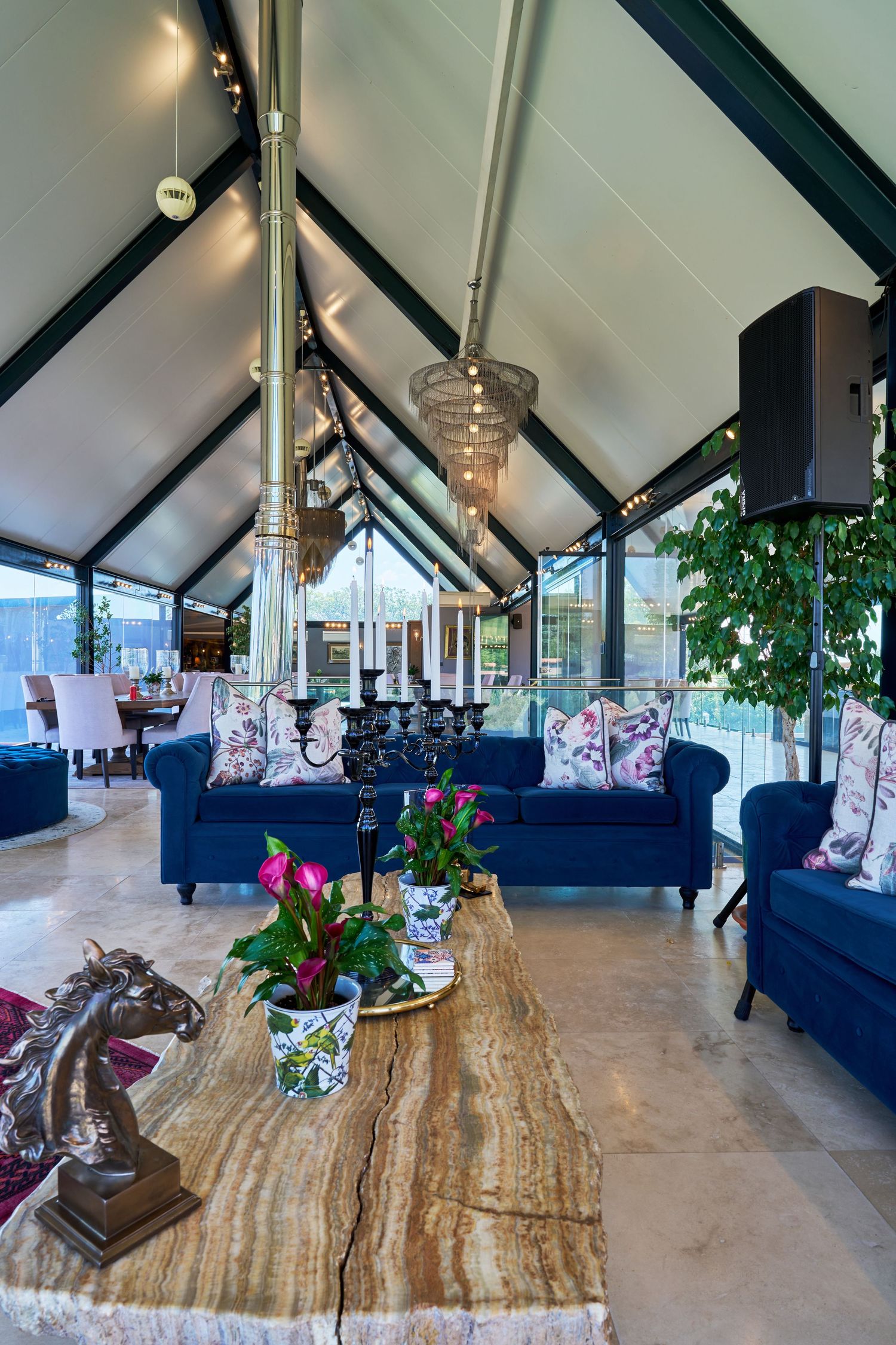 Spacious event venue with vaulted black beam ceiling, navy blue sofas, and live edge marble coffee table.