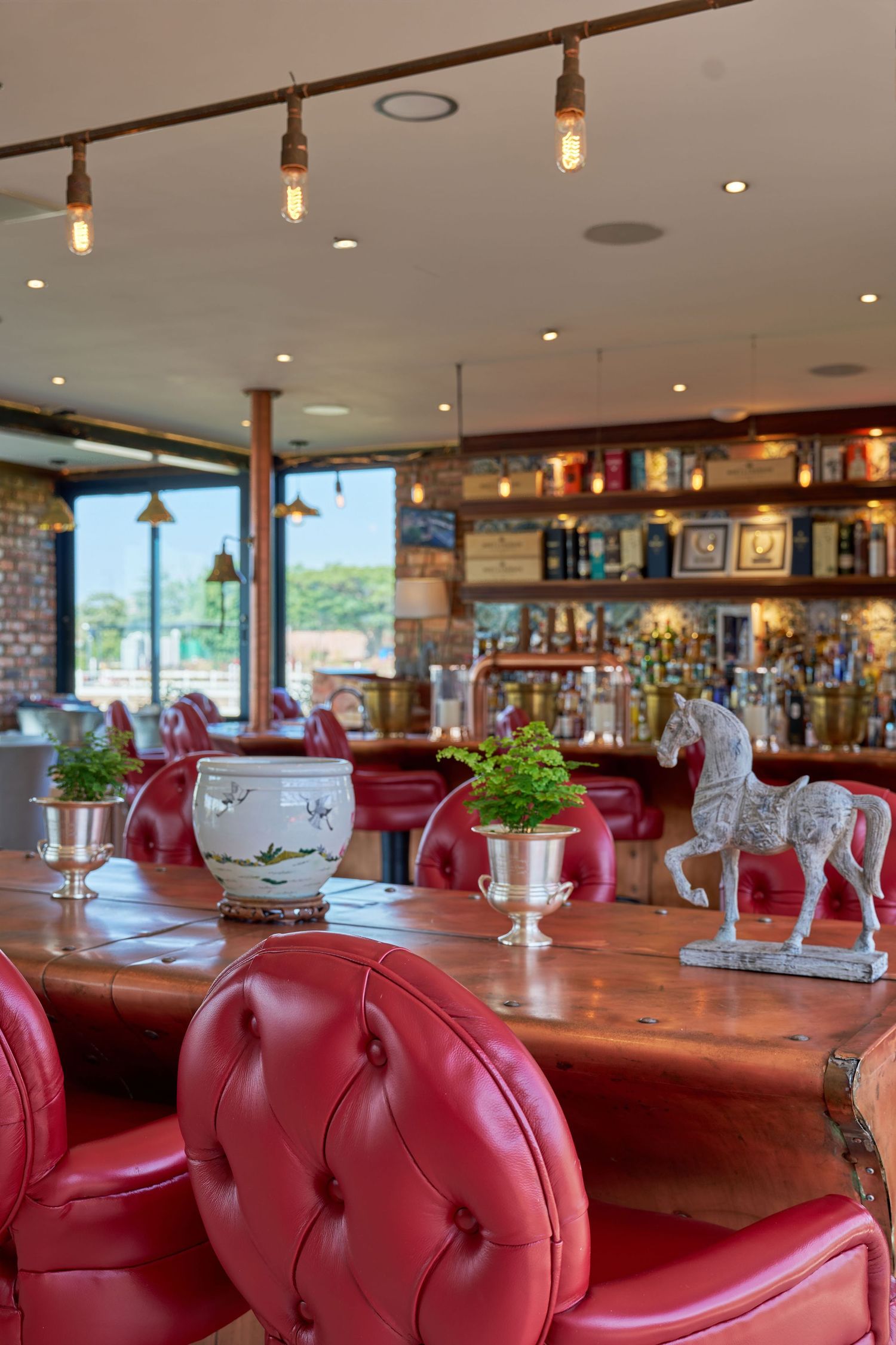 Elegant restaurant interior with red tufted leather chairs, wooden tables, and a well-stocked bar.
