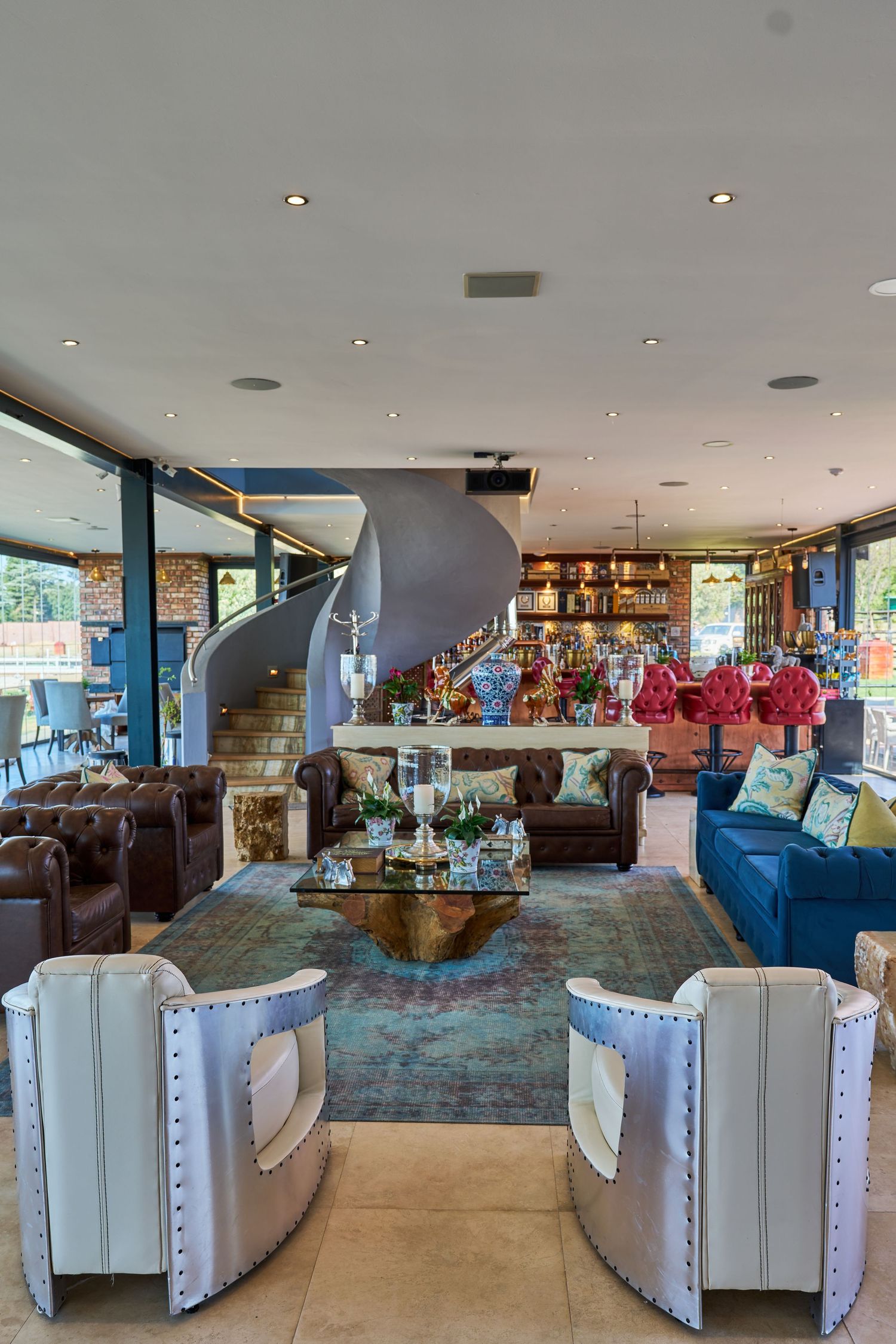 Sophisticated open-plan lounge with spiral staircase, blue sofa, leather chairs, and eclectic decorative accents.