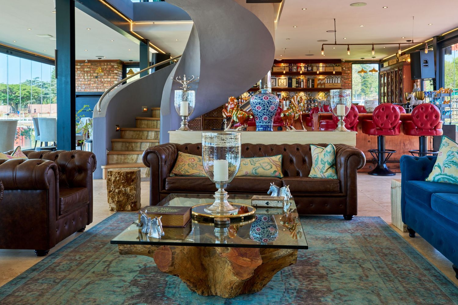 Elegant hotel lobby featuring leather sofas, a glass coffee table, spiral staircase, and vibrant red floral decor.