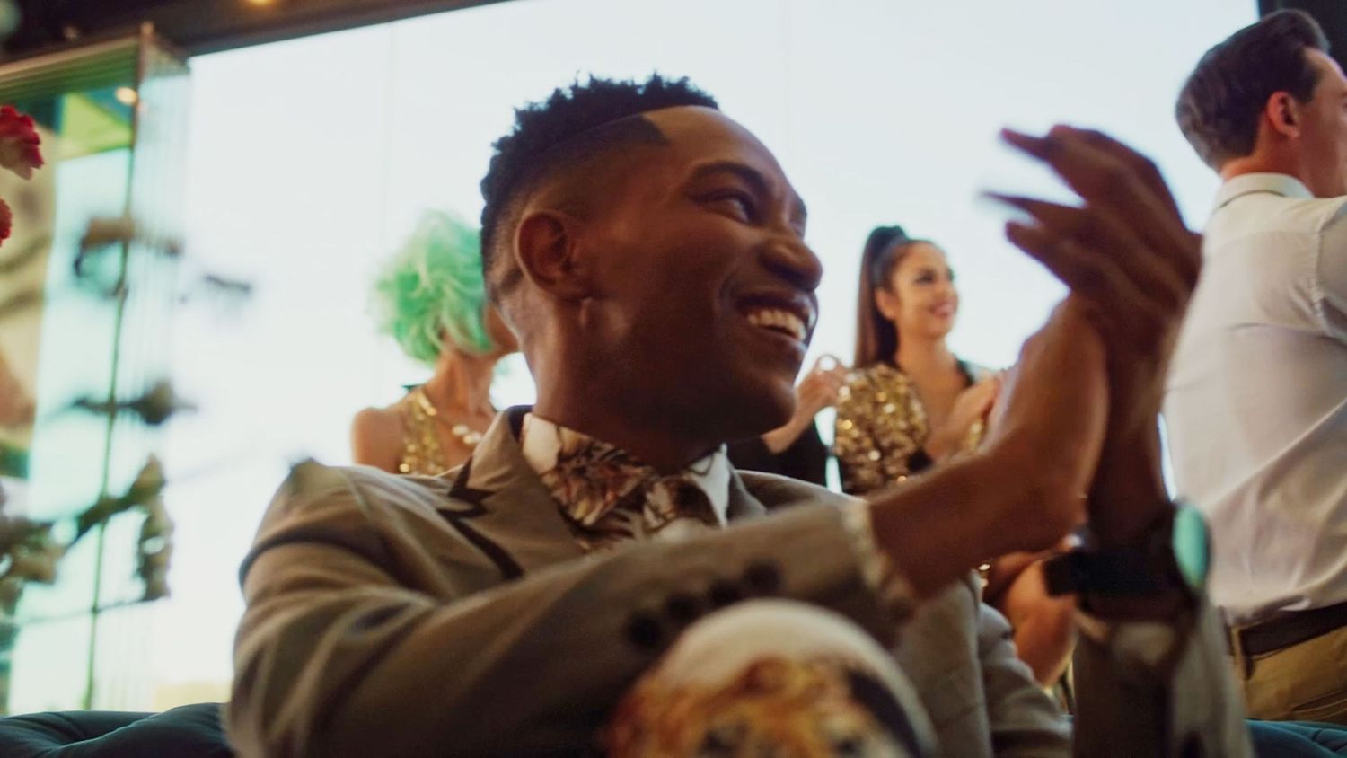 Smiling man in a grey suit with floral bow tie clapping at a festive celebration event.