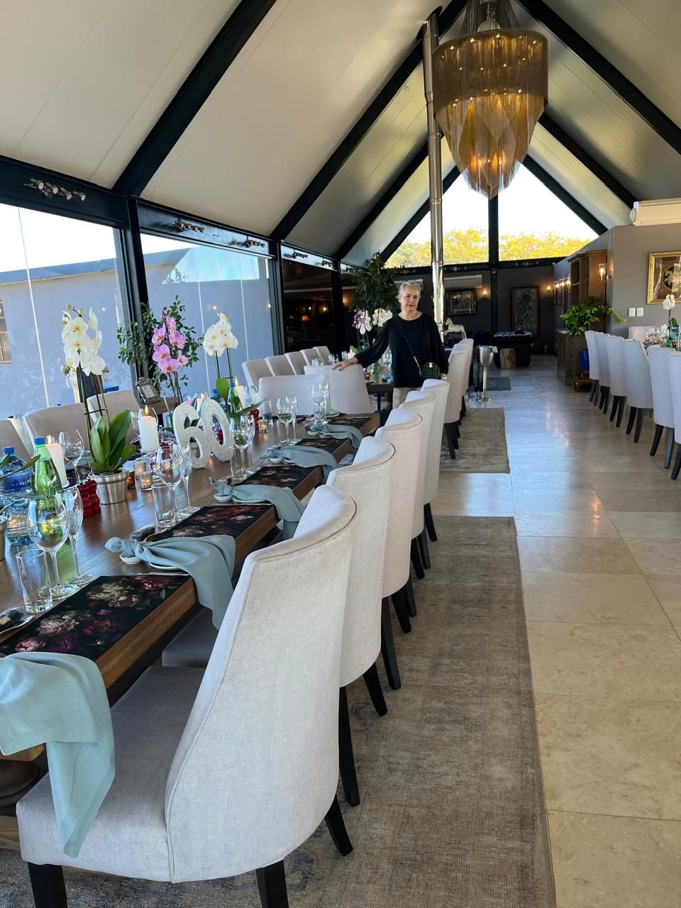 Long elegant dining room with floral table settings, crystal glasses, and a gold chandelier overhead.