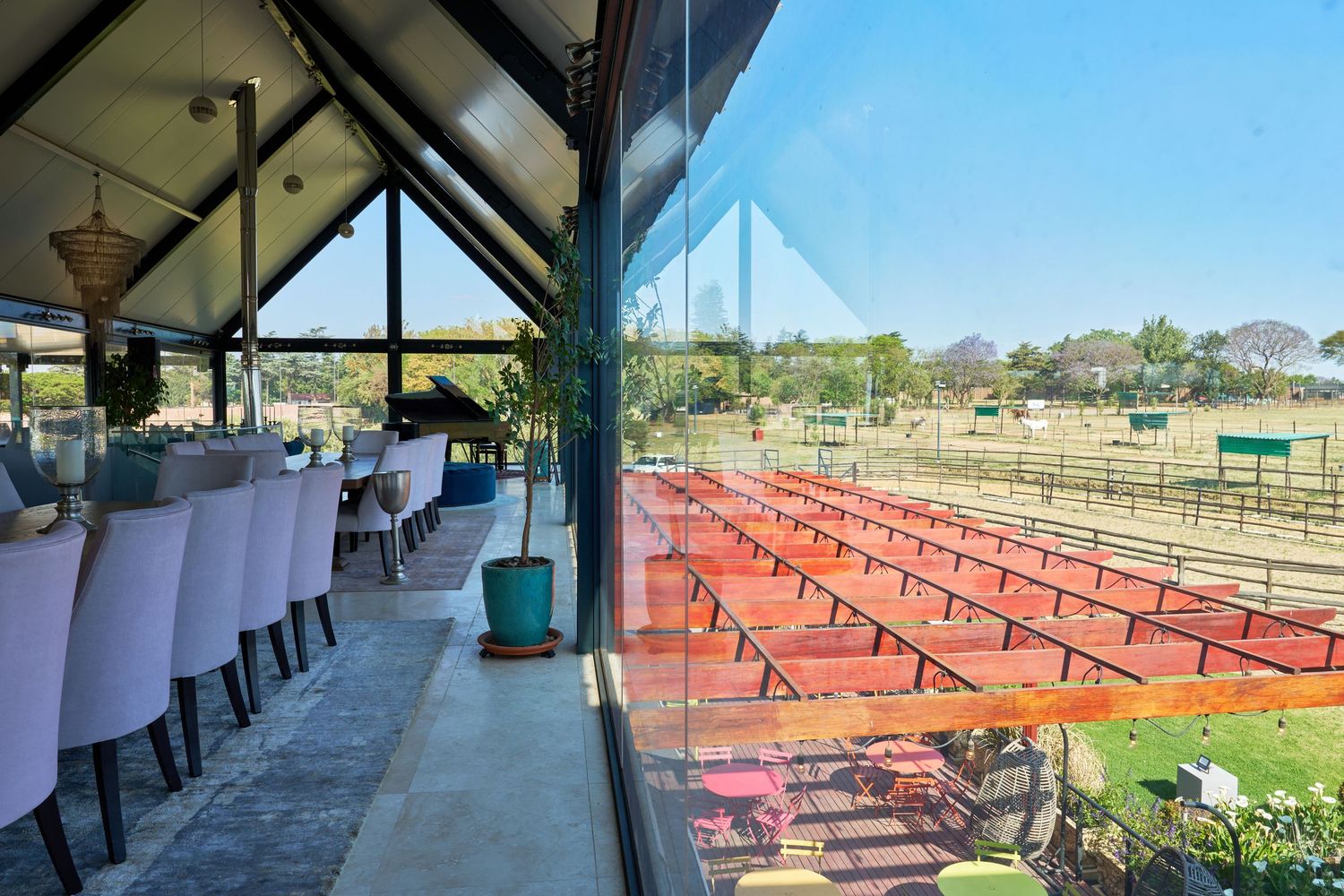 Glass-walled venue overlooking red stadium seating and an open equestrian field under a clear sky.