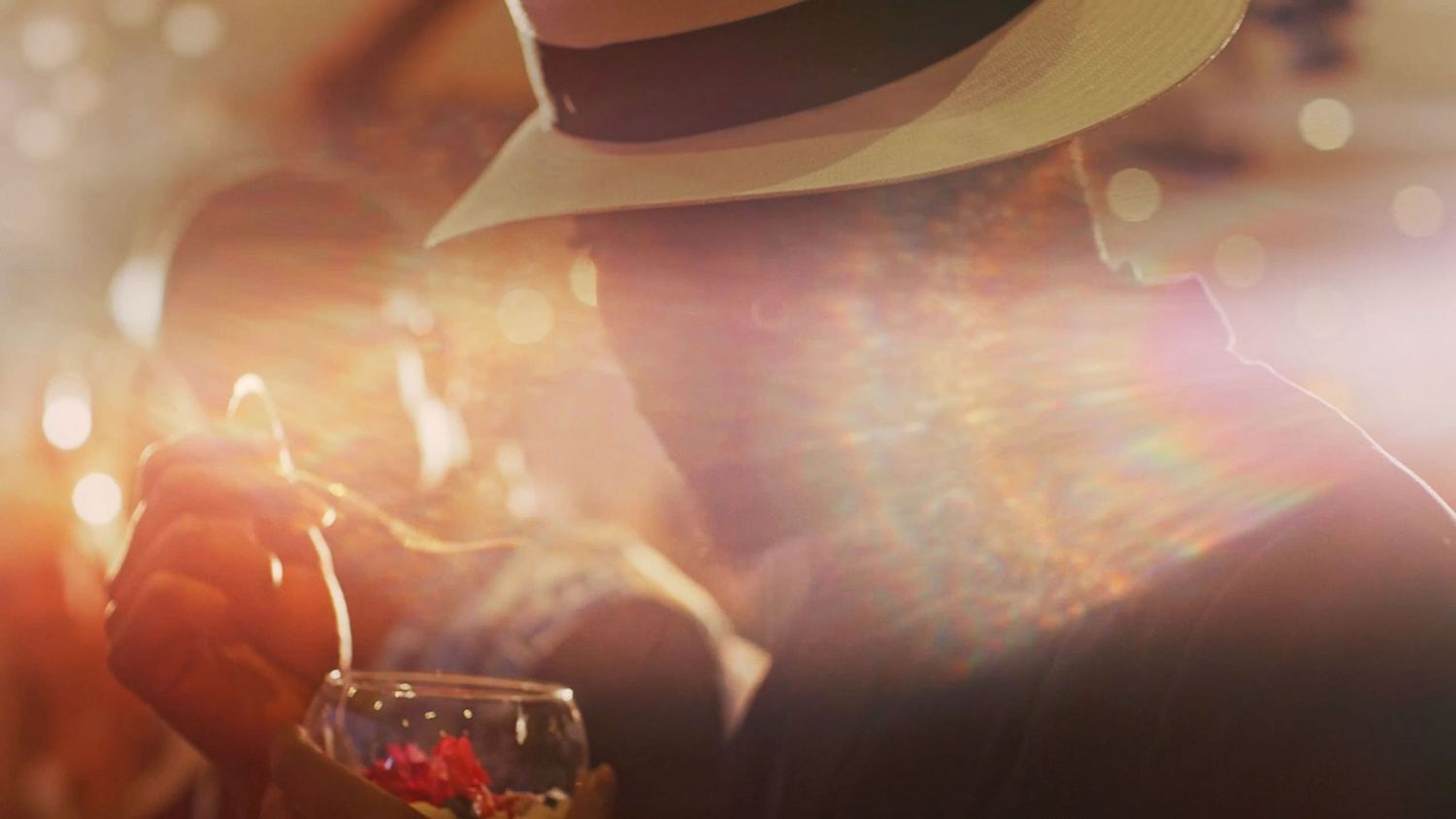 Atmospheric close-up of a person wearing a fedora hat in warm golden bokeh lighting at an event.
