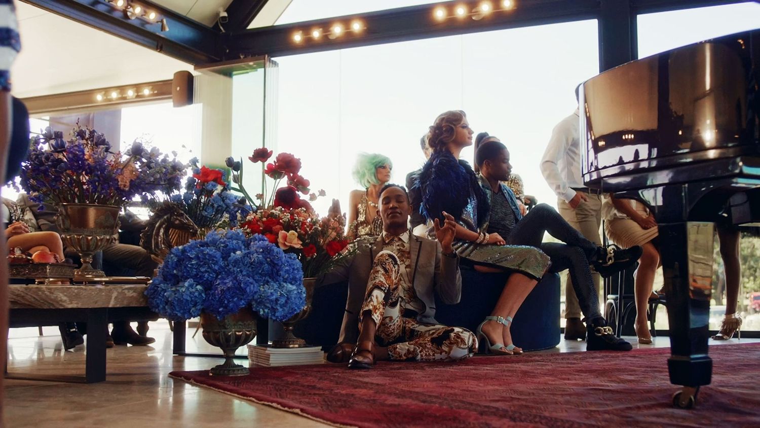 Guests relaxing among colorful floral arrangements in a luxurious sunlit venue interior.