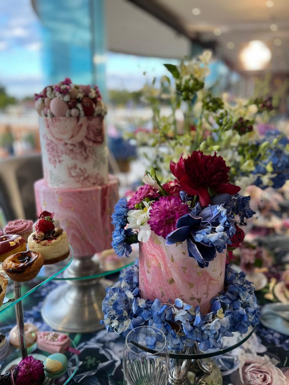 Elegant pink marble wedding cakes adorned with fresh blue hydrangeas and red flowers on a dessert table.