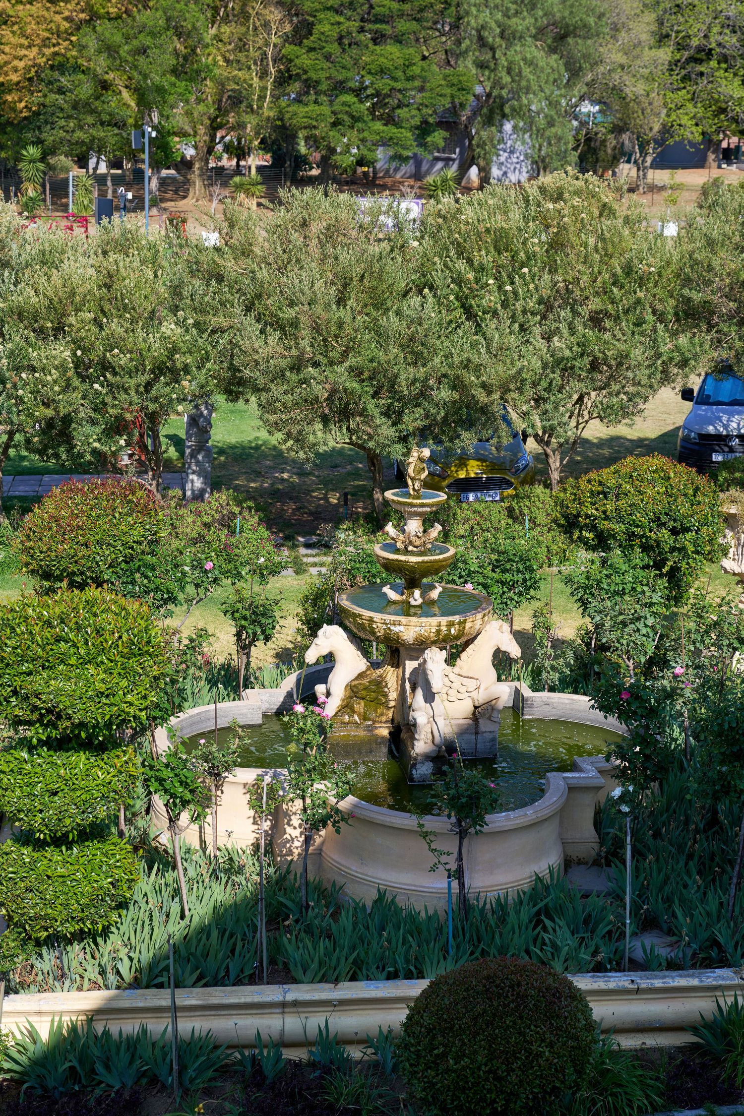 Aerial view of an elegant tiered garden fountain surrounded by manicured hedges and lush green landscaping.