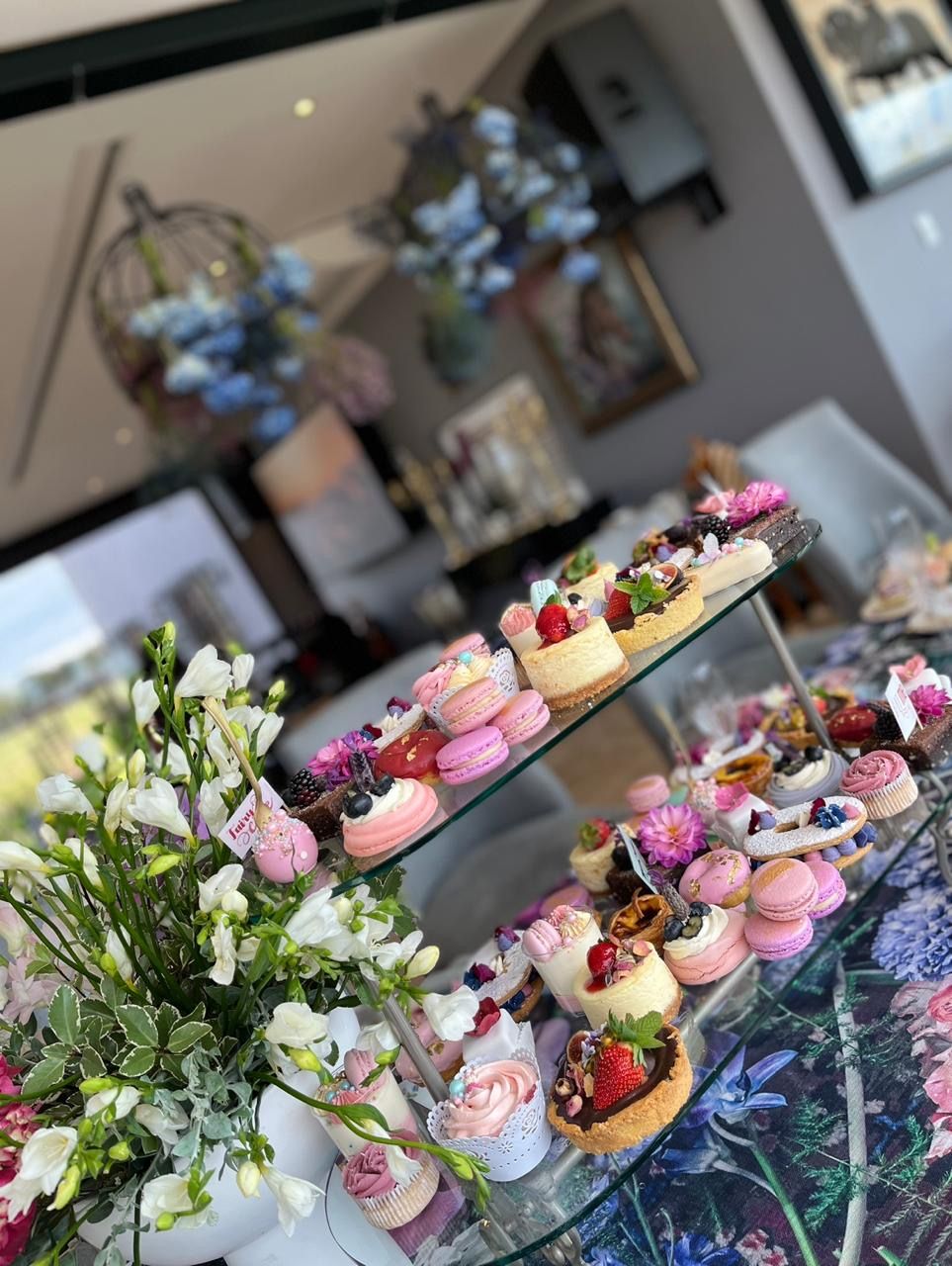 A tiered glass stand filled with macarons, cheesecakes, tarts, and cupcakes at an elegant high tea dessert display.