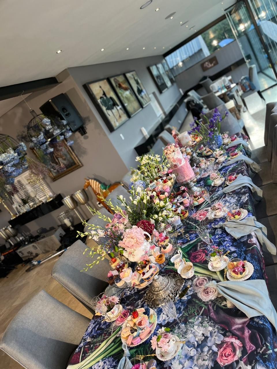 Long dining table adorned with colorful pink and purple floral arrangements in modern venue.