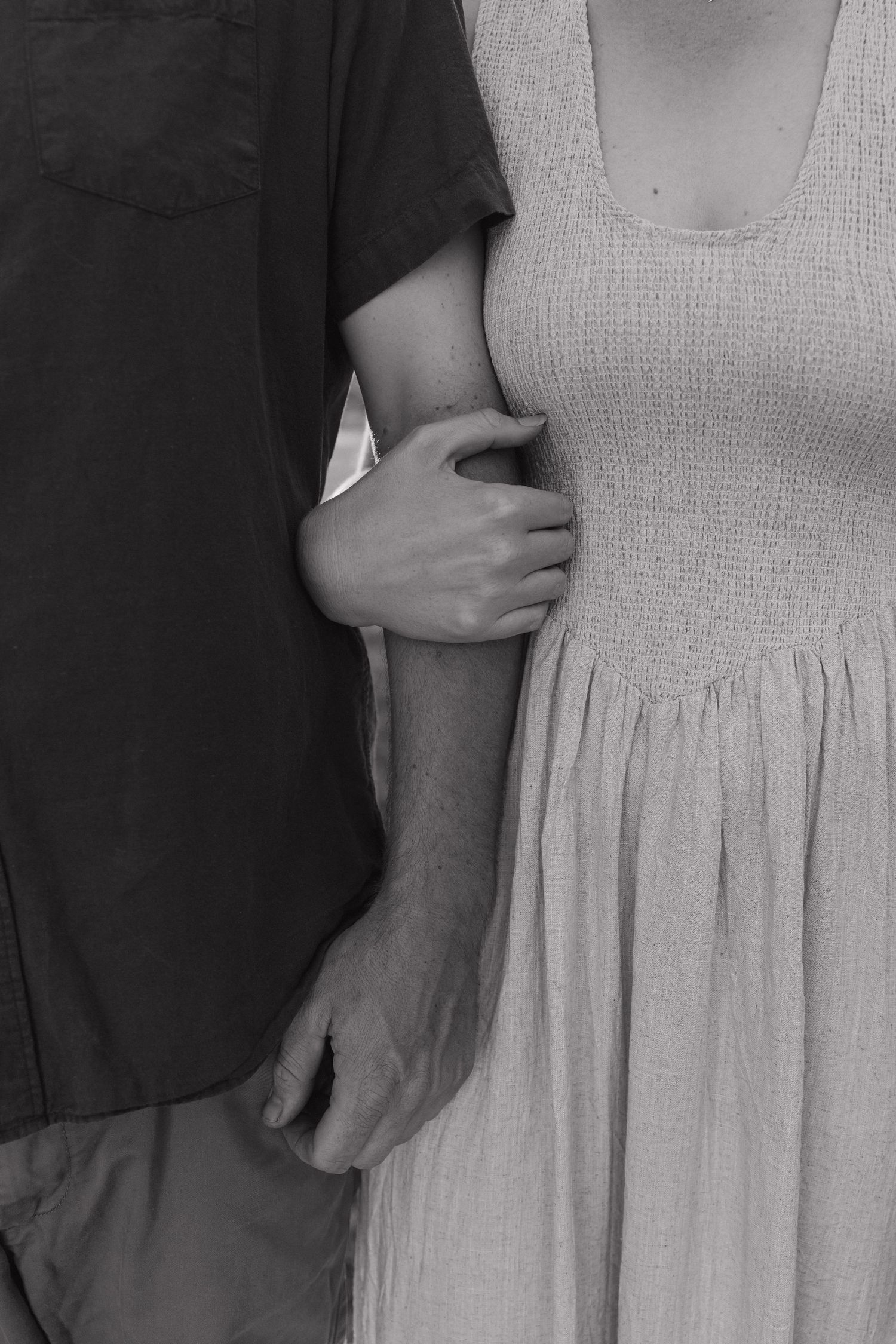 Black and white photo of a couple standing close together, woman in smocked dress holding mans arm affectionately. Bundaberg photographer