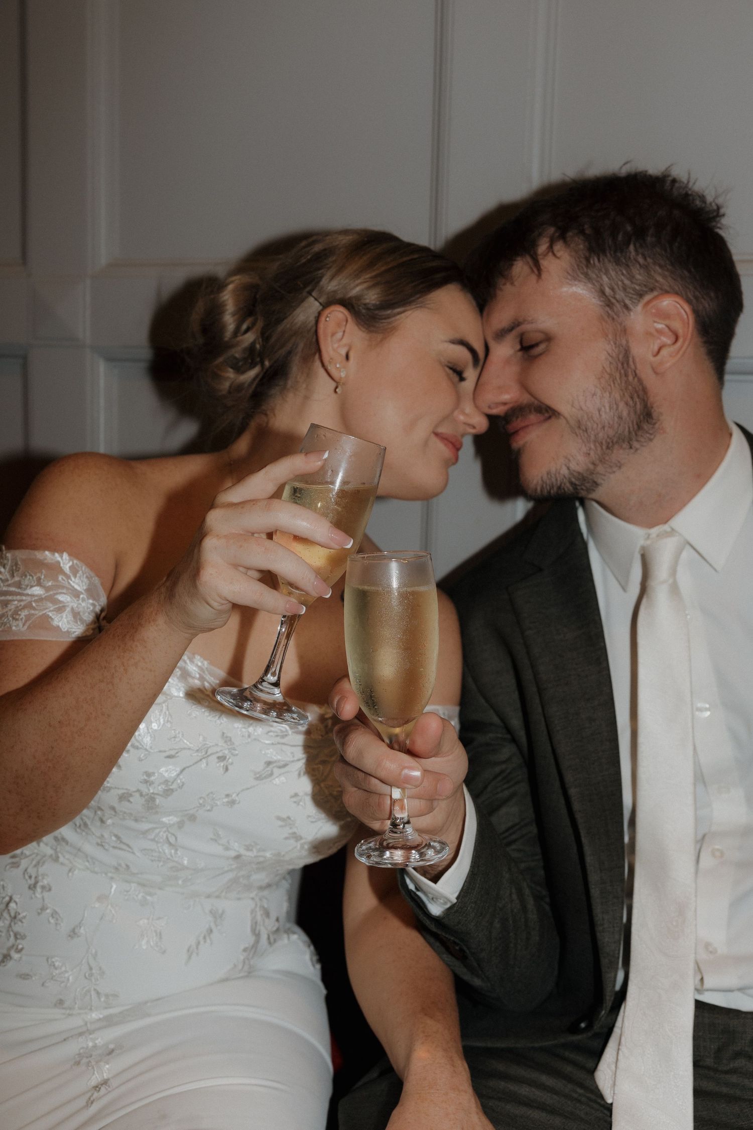 Bride and groom in wedding attire toasting with champagne glasses, foreheads touching in a romantic moment. Bundaberg Photographer
