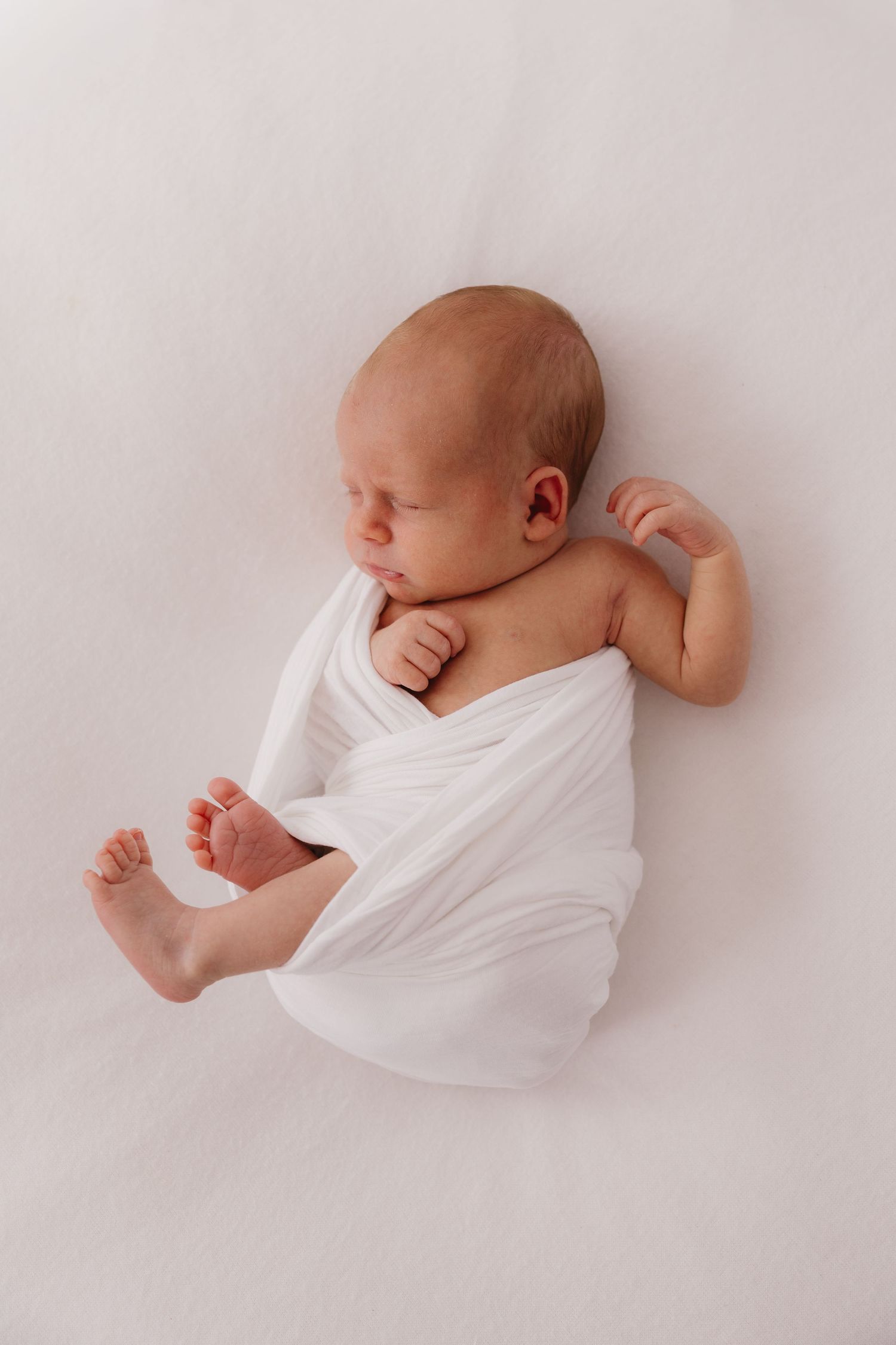 Peaceful newborn baby sleeping wrapped in a white swaddle blanket on a soft white background. Bundaberg photographer
