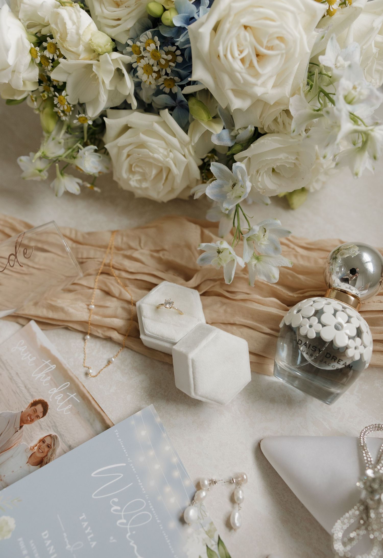 Elegant wedding flat lay with white roses, ring box, pearl earrings, perfume, and blue florals. Bundaberg photographer