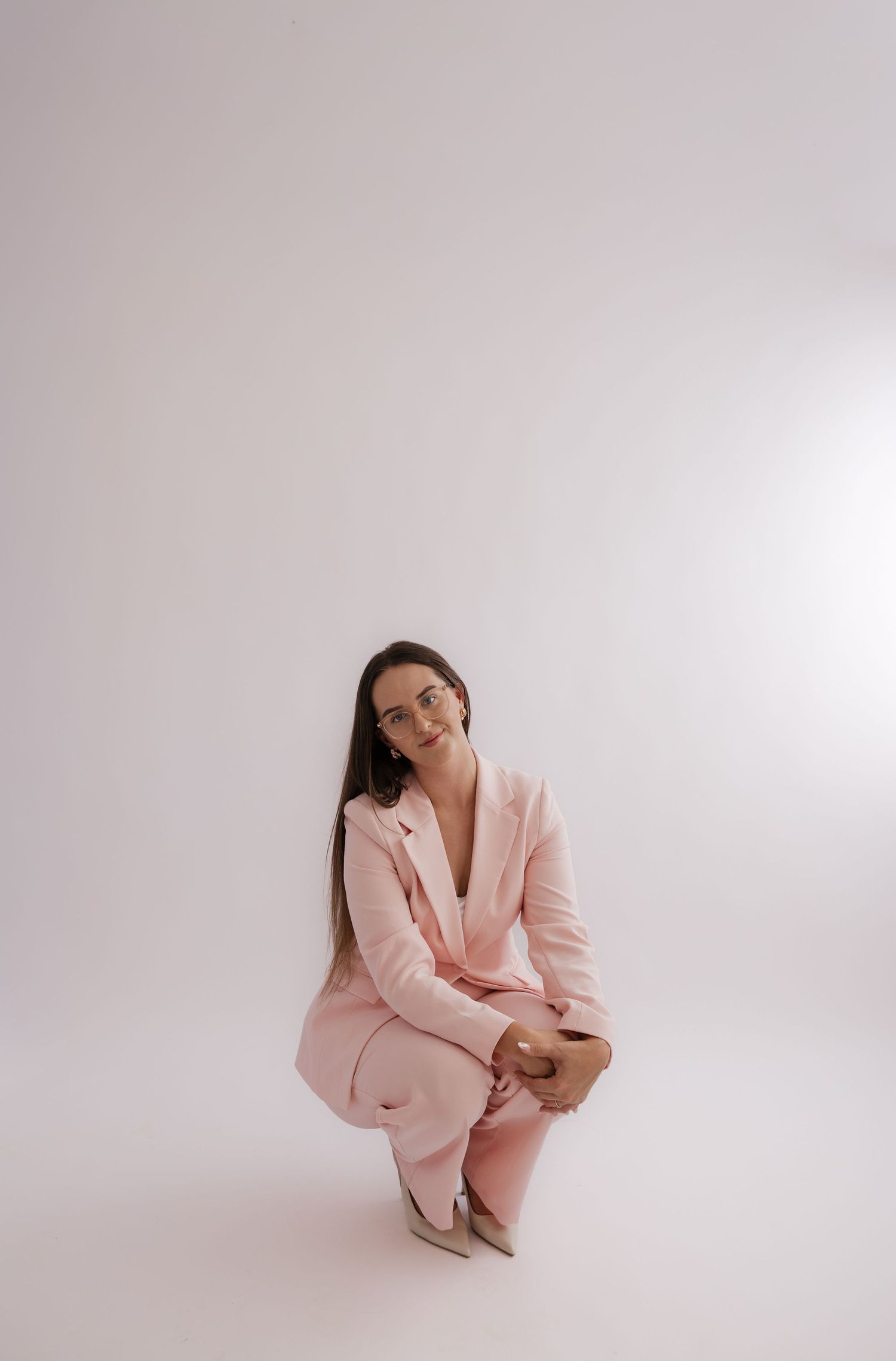Woman in pink pantsuit crouching gracefully against white background, smiling confidently at camera. Bundaberg photographer
