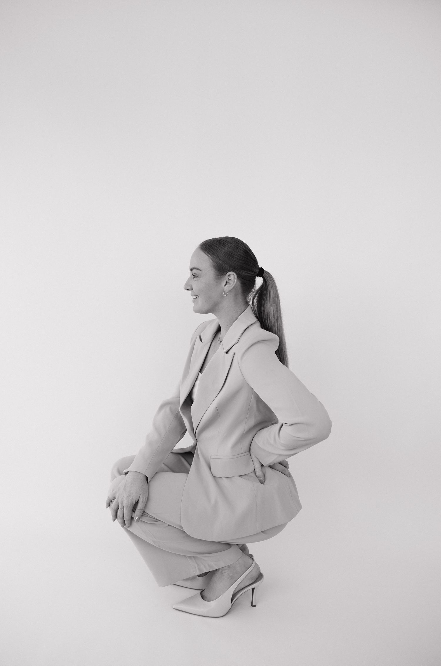 Woman in tailored suit squatting gracefully, black and white fashion portrait on white background. Bundaberg photographer