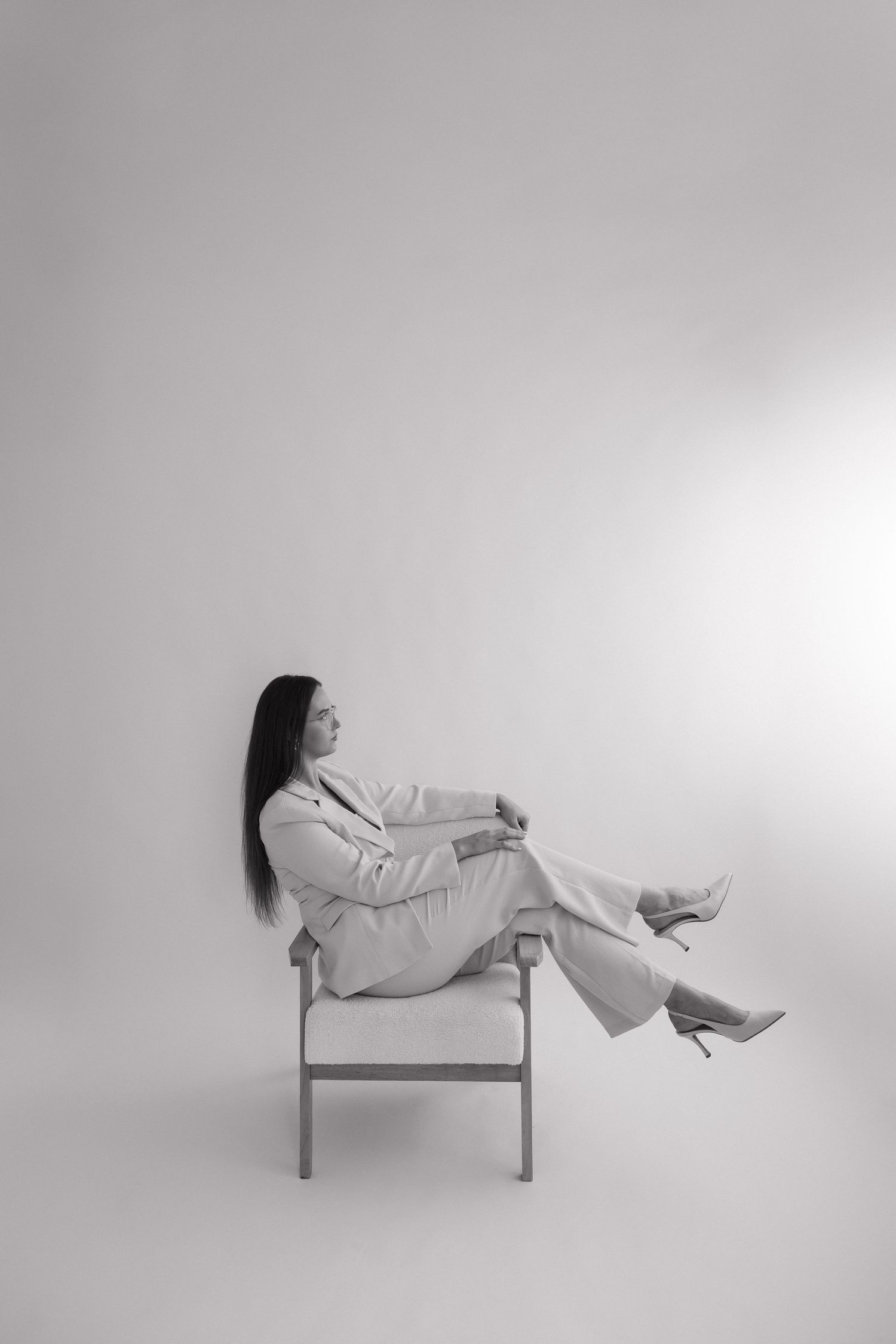 Black and white photo of a woman in a pantsuit sitting elegantly in a chair with legs raised. Bundaberg photographer Branding