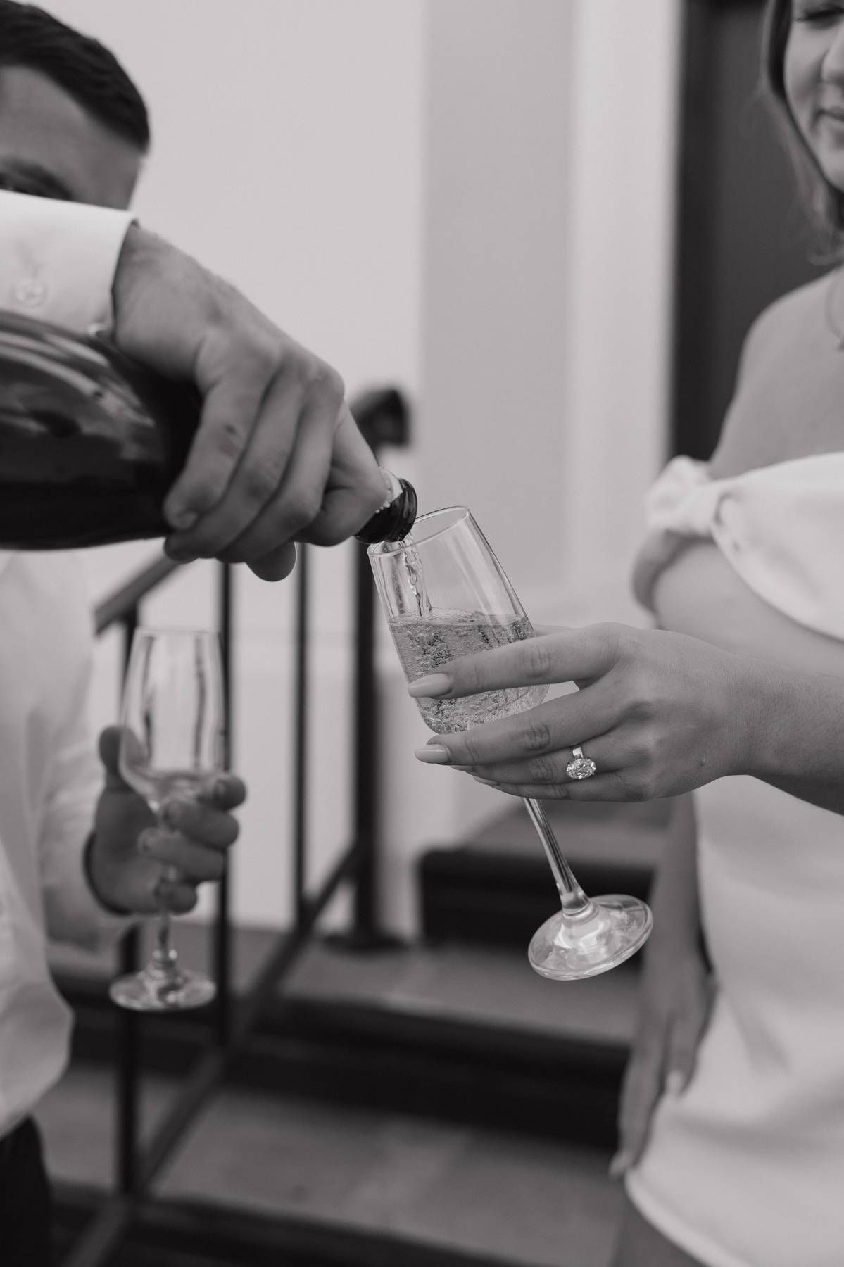 Black and white photo of a man pouring champagne into a wine glass held by a woman at a celebration. Bundaberg Photographer