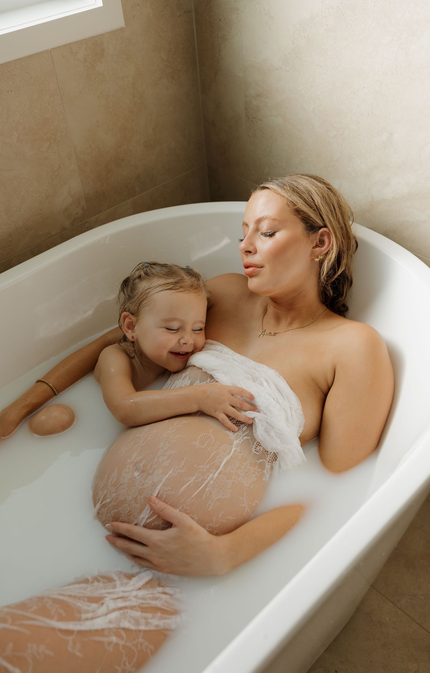 Pregnant woman relaxing in a milk bath with her young daughter, sharing a tender moment together. Bundaberg Photographer