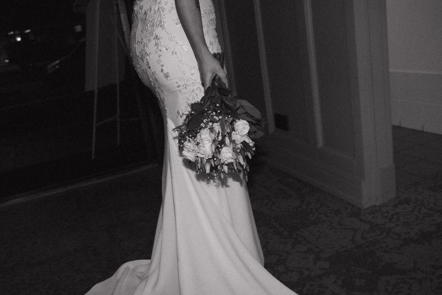 Black and white photo of a bride in a fitted lace wedding gown holding a floral bouquet.  Bundaberg Photographer