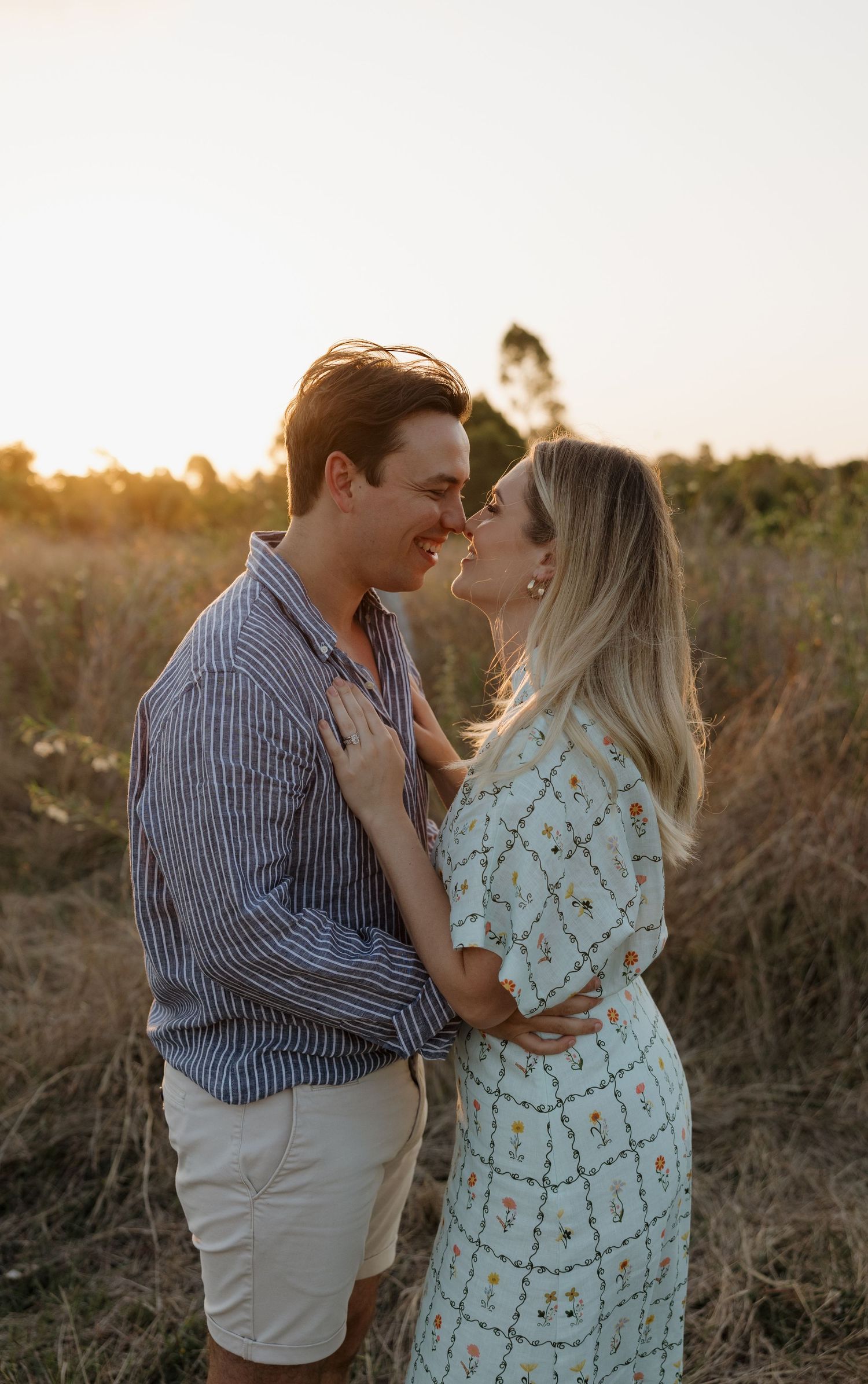 Couple sharing a romantic moment at golden hour in a field, man in striped shirt and woman in floral dress. Bundaberg photographer