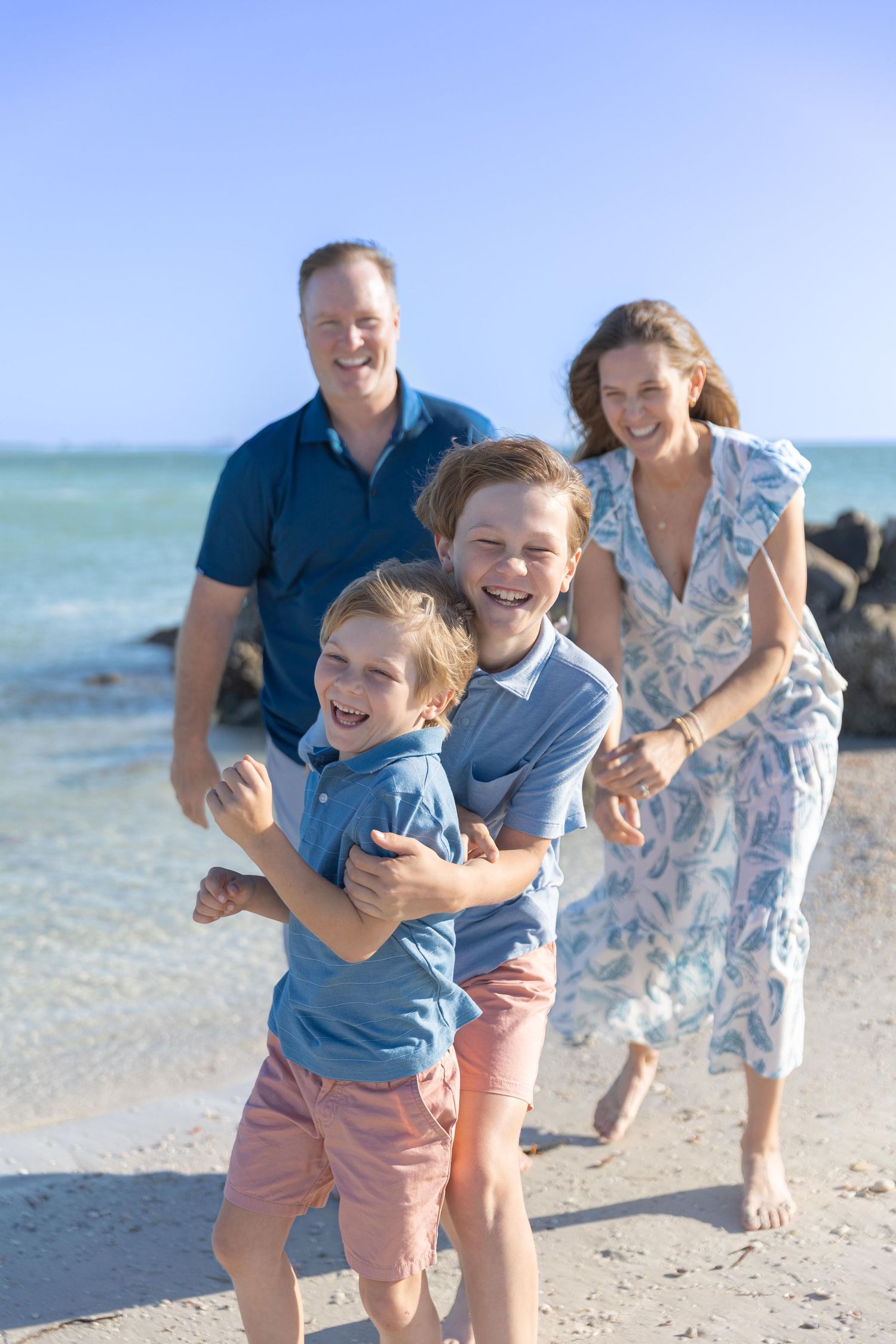 A happy family enjoying a sunny day at the beach with turquoise water and rocky shoreline in the background.