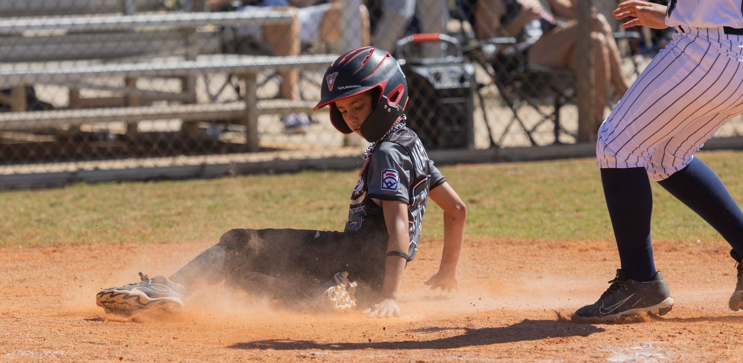 Baseball player sliding into base creating a cloud of dust during an intense game play.