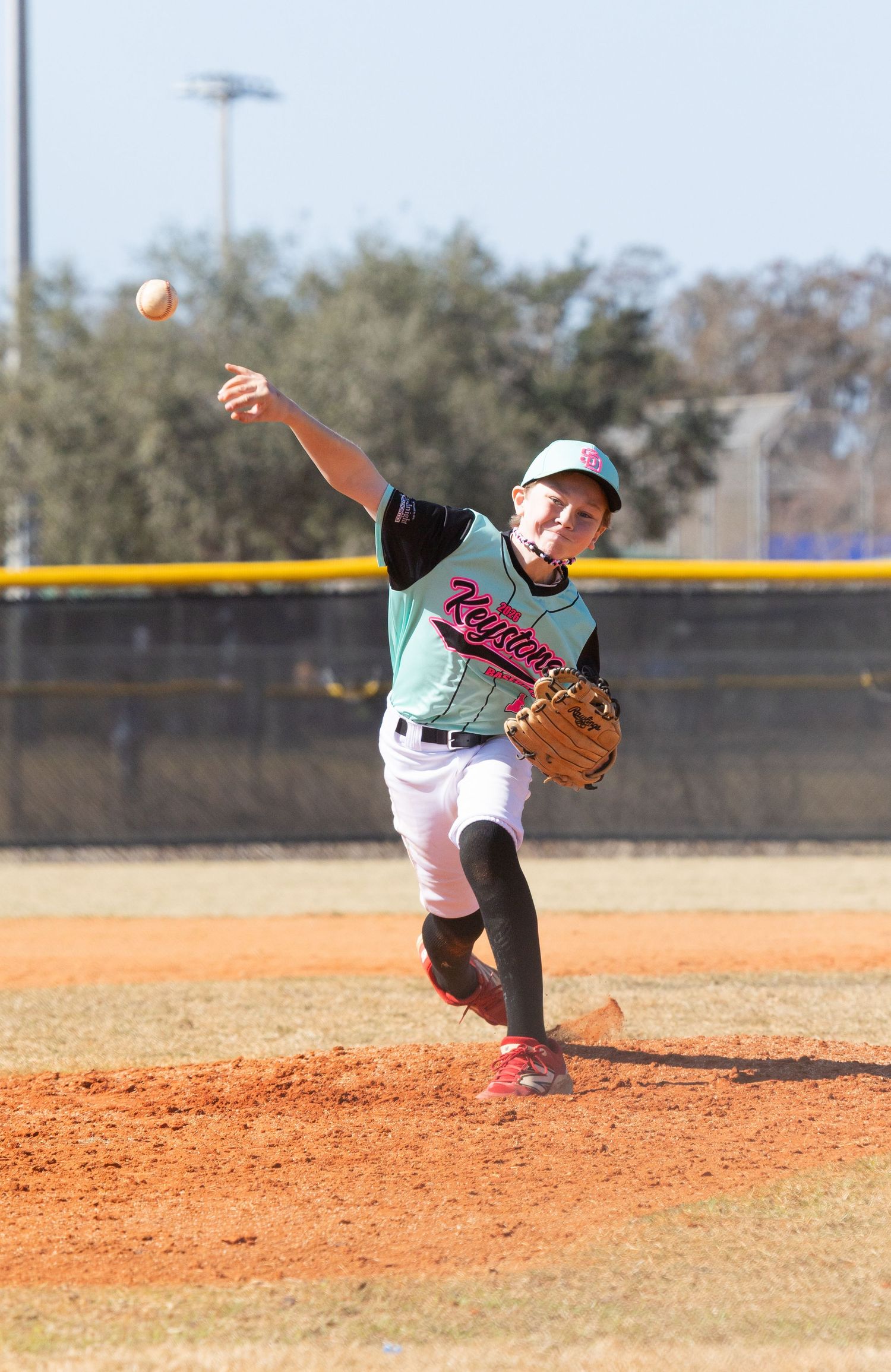 Baseball pitcher in mint green uniform mid-delivery on dirt mound.