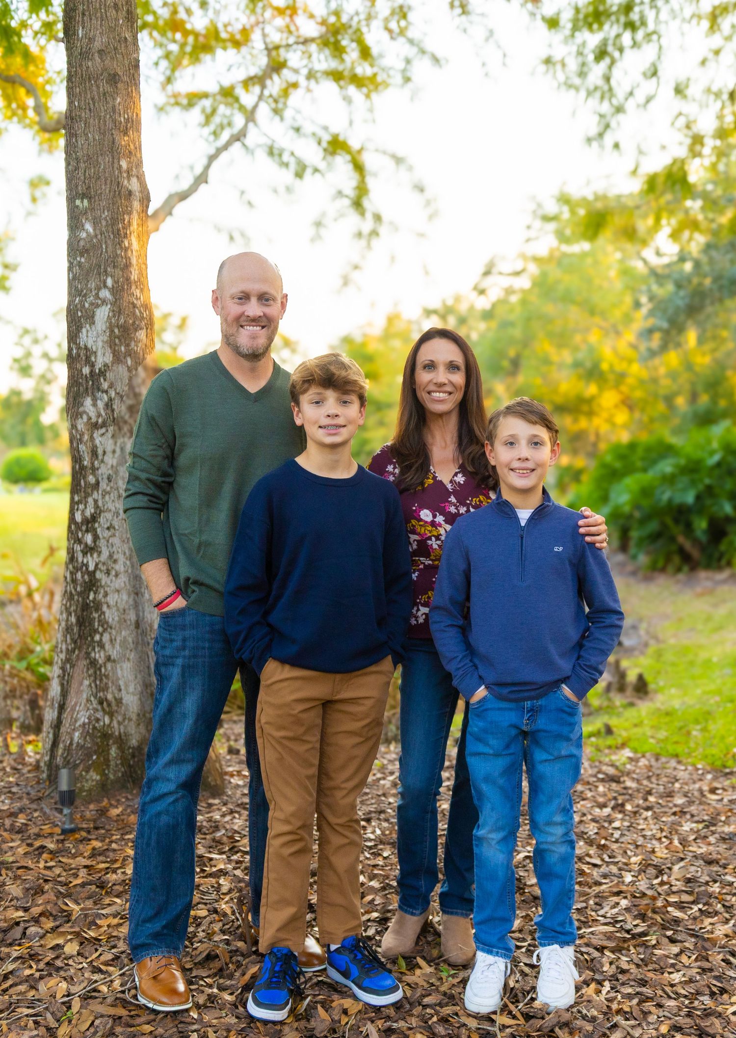 Family poses together on fallen autumn leaves in a park setting during golden hour.