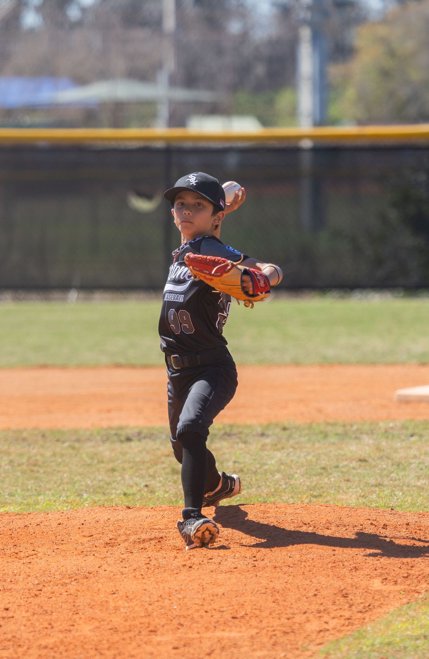 Youth baseball player fields ground ball in defensive stance on dirt infield.