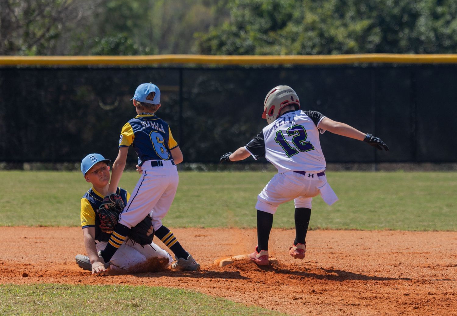 Baseball players in action during game with runner sliding into base while fielder prepares to catch.