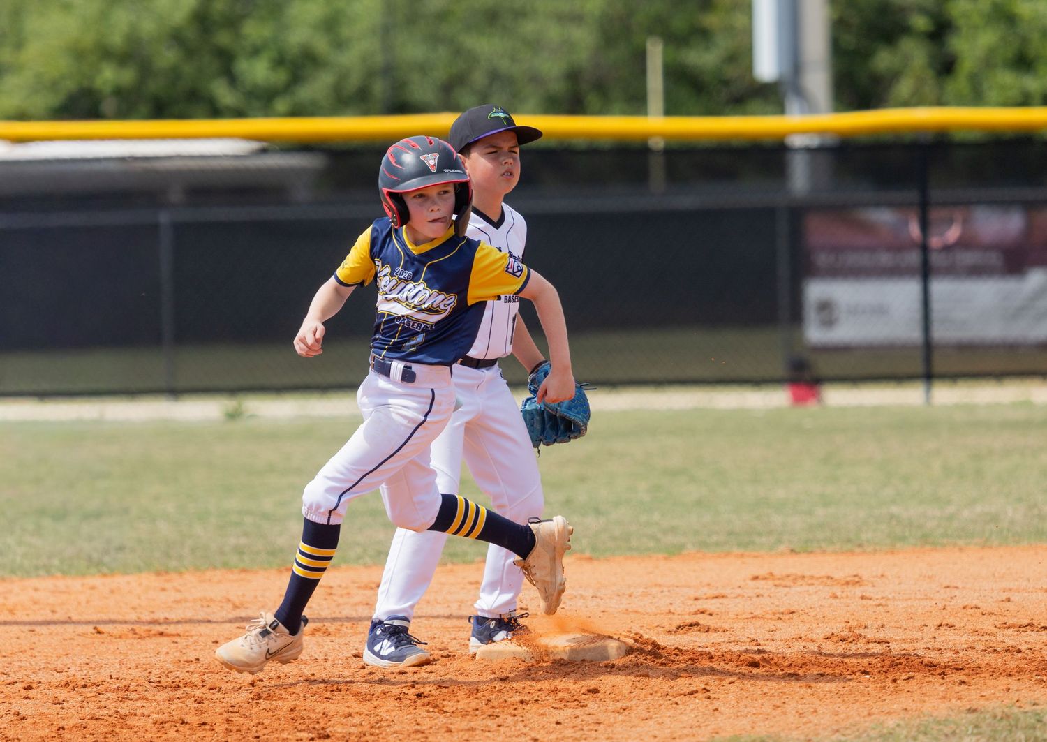 Baseball players in action with runner leading off base while being closely watched.