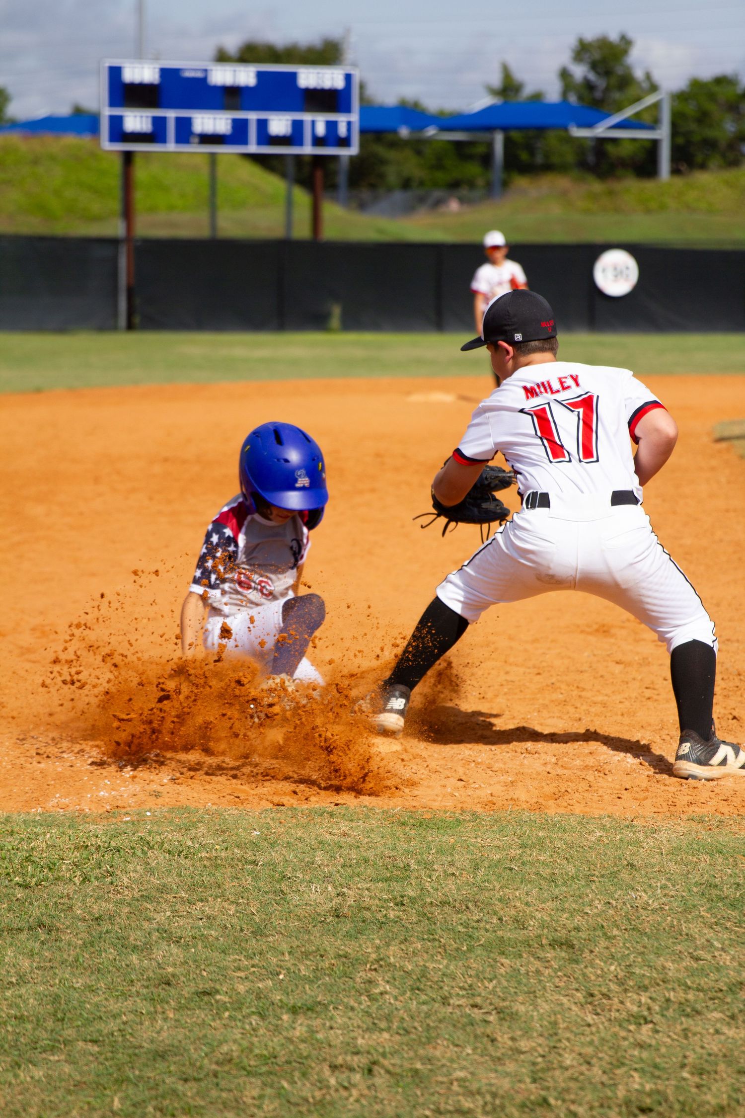 Baseball player slides into base creating a cloud of dirt on the infield during an intense game.