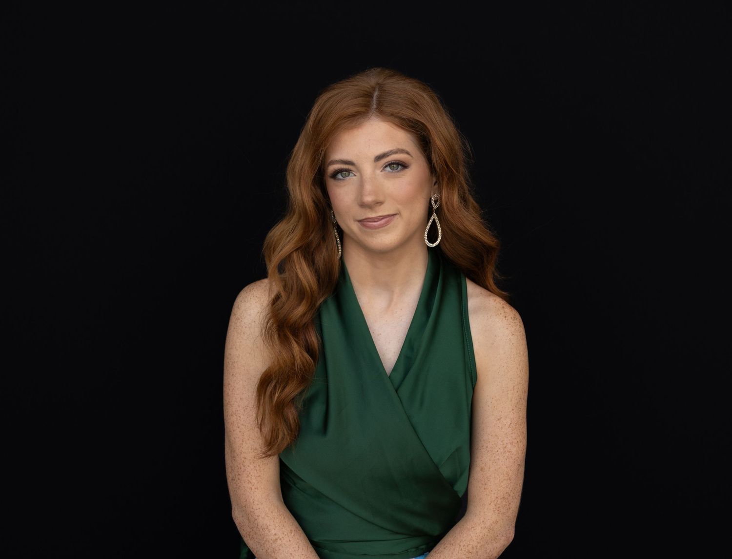 Woman with red hair in green dress poses against dark background, wearing silver earrings.